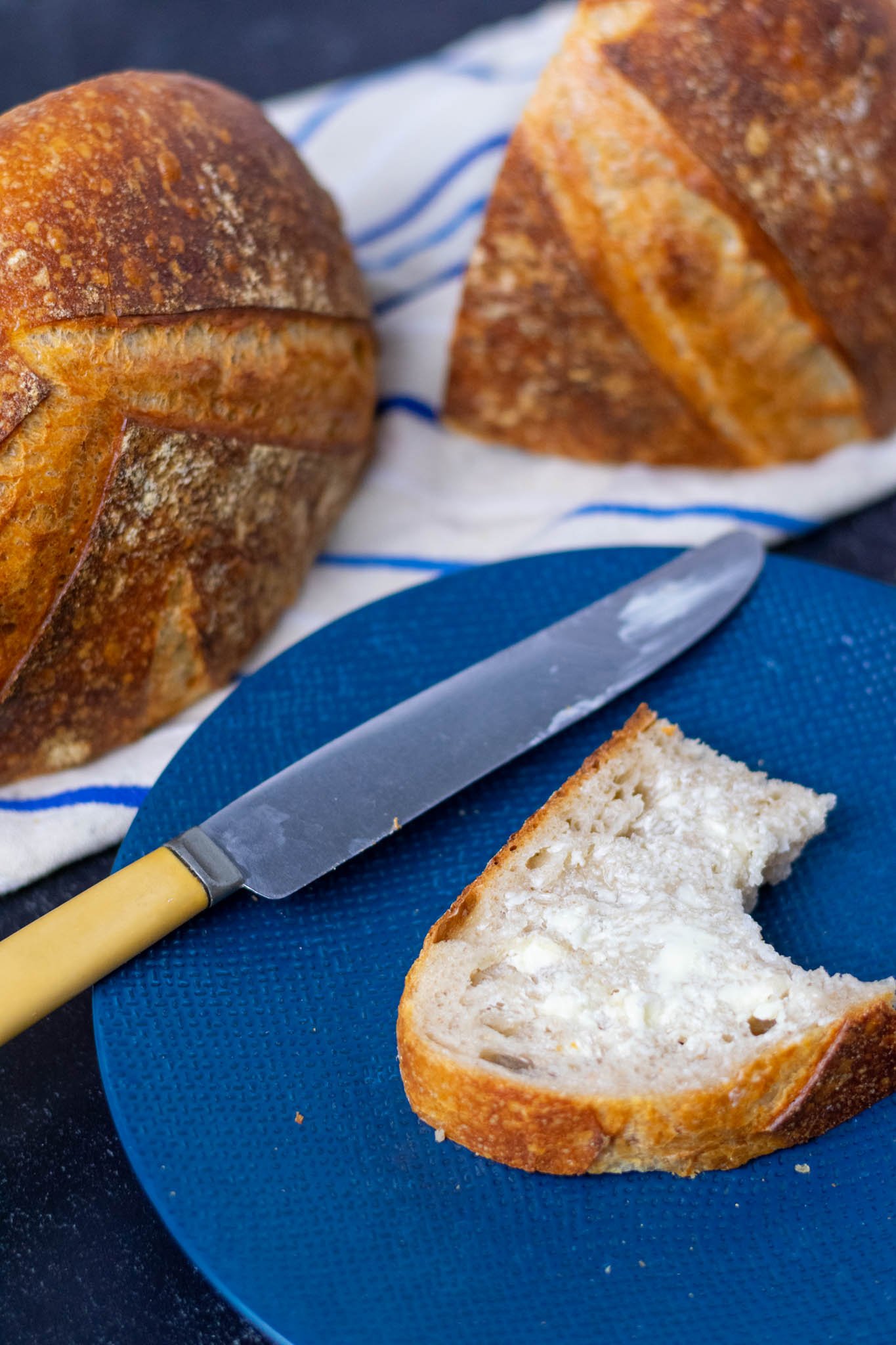 Slice of my everyday sourdough bread with butter and a butter knife on a plate