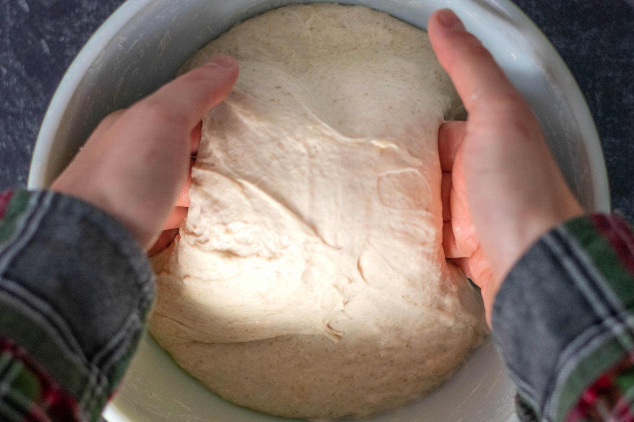 Hands lifting middle of dough to perform a coil fold