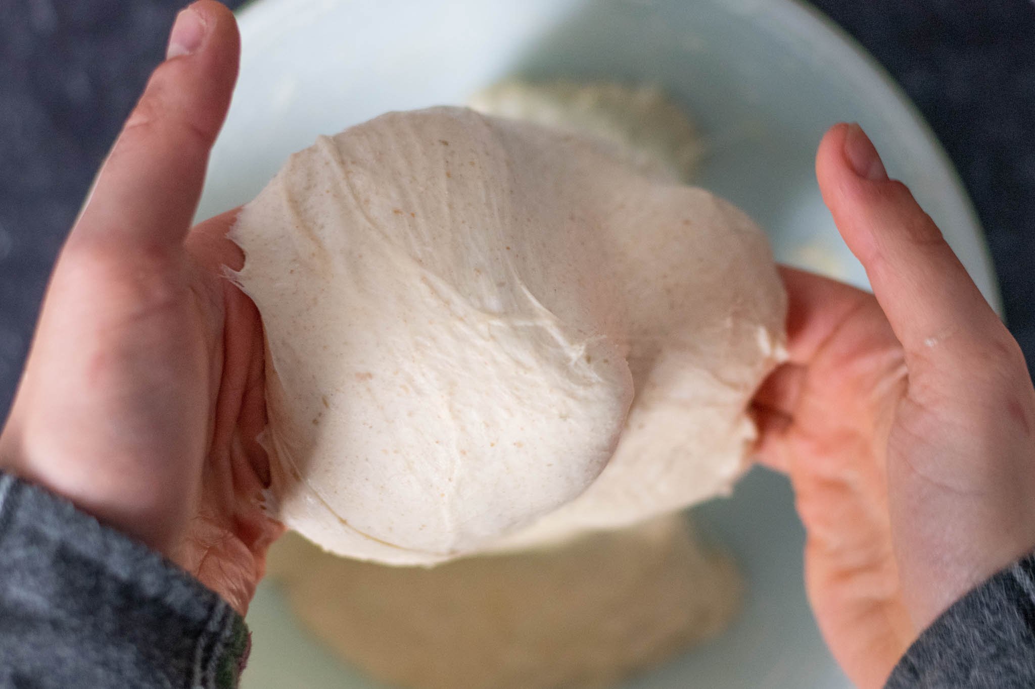 Hands lifting middle of dough high to perform a coil fold