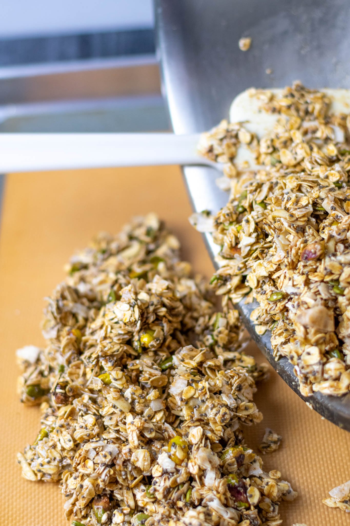 Spatula pouring sourdouogh discard granola onto sheet pan