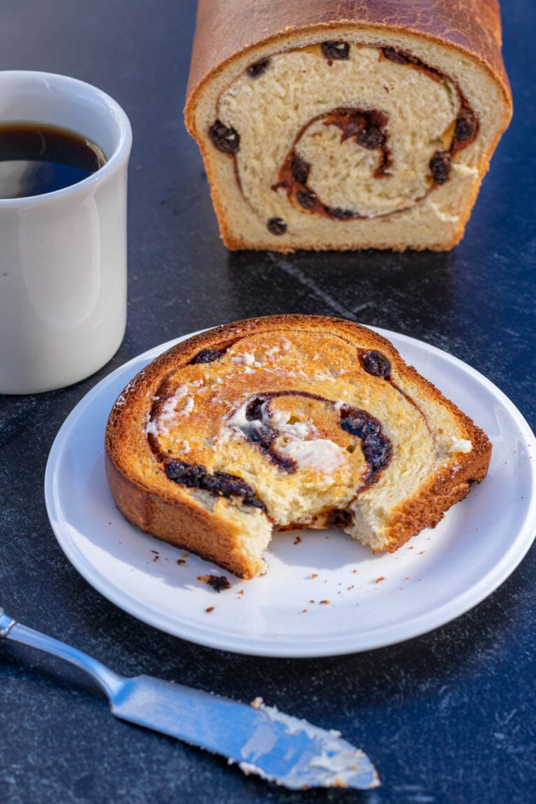 Bite of toasted sourdough cinnamon raisin swirl bread on plate with butter and coffee