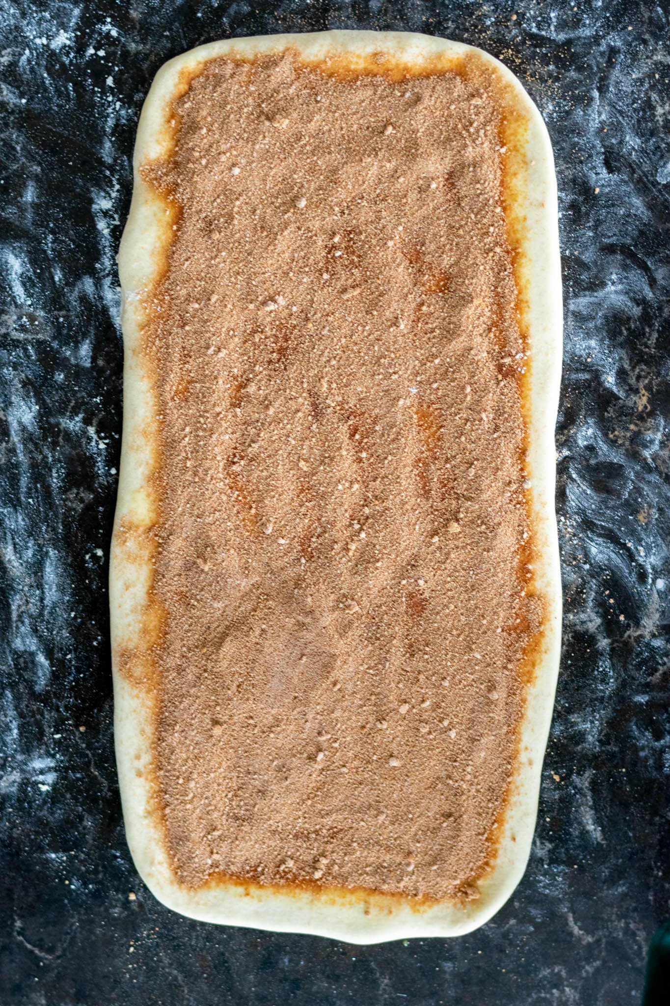 Cinnamon sugar mixture filling added on top of dough on floured counter