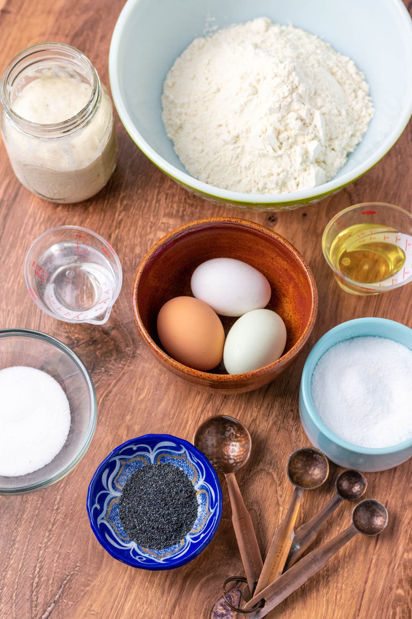 Ingredients needed for sourdough challah: levain, flour, eggs, oil, water, poppy seeds, sugar, and salt