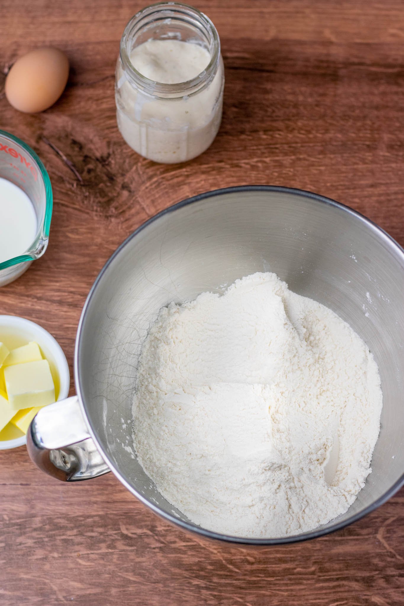 Dry ingredients of flour, sugar, and salt mixed together in bowl with wet ingredients in background