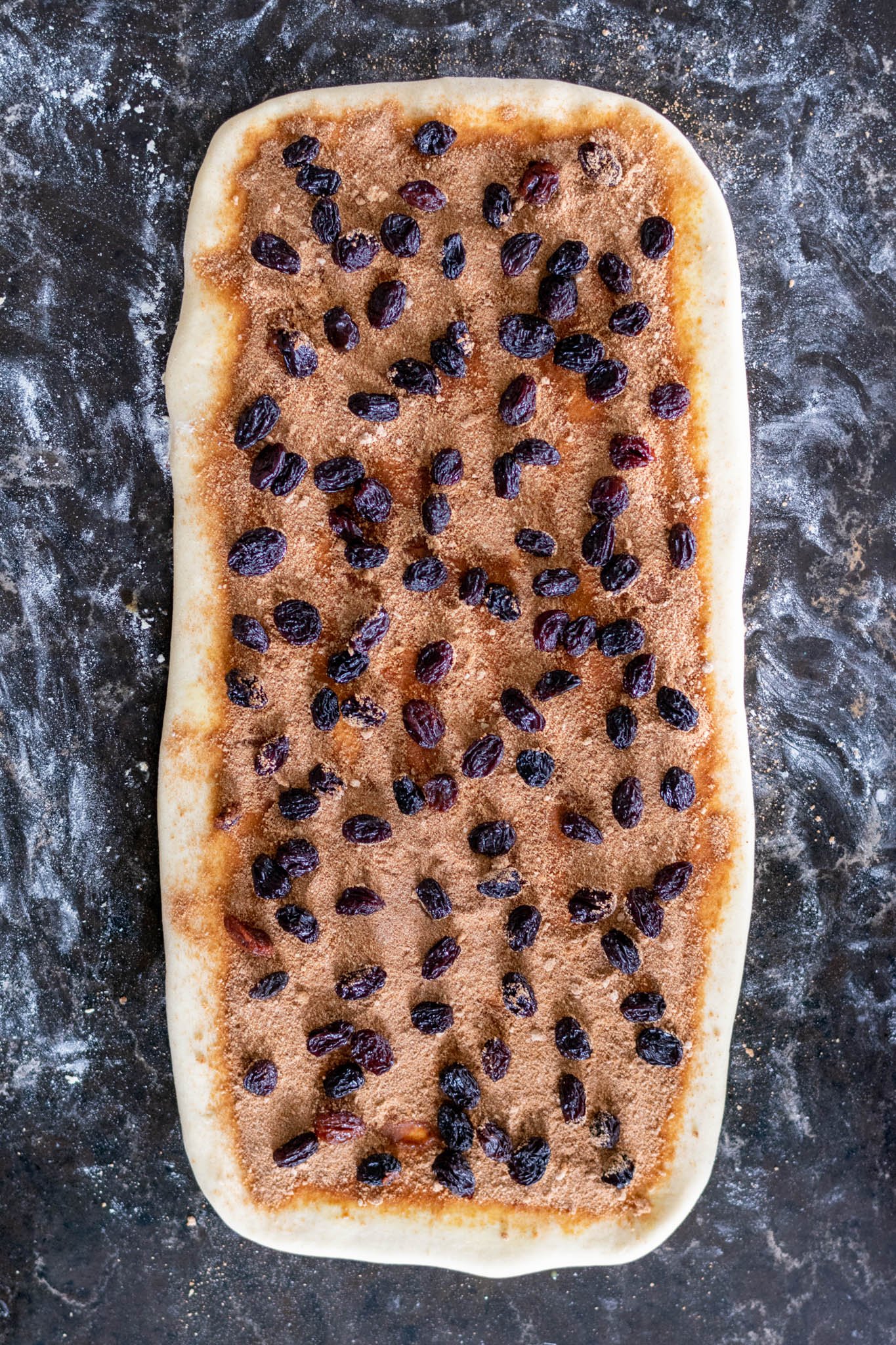 Overhead of raisins added to rolled out bread dough on counter with filling