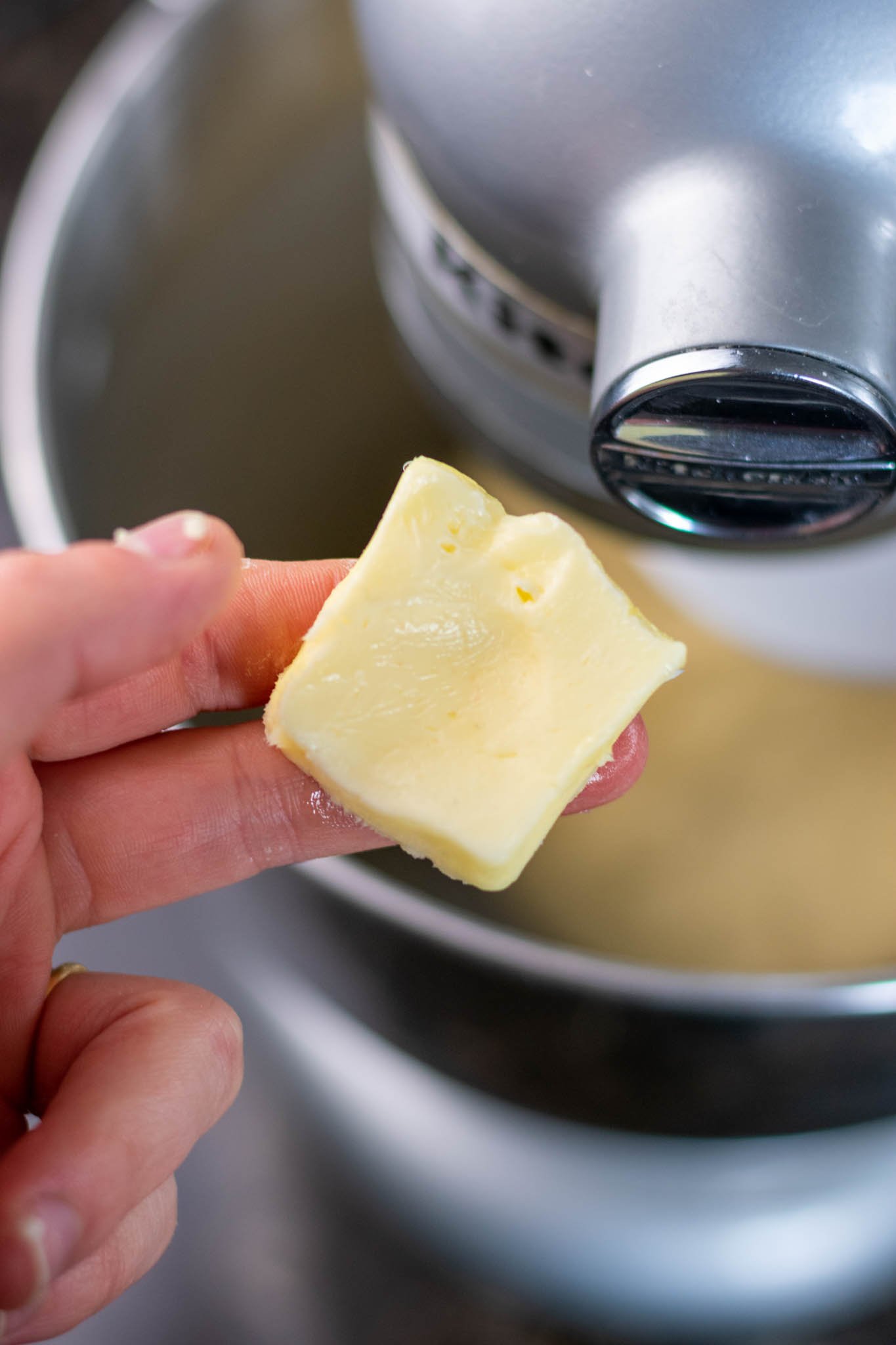 Hand holding softened butter with indentation over stand mixer