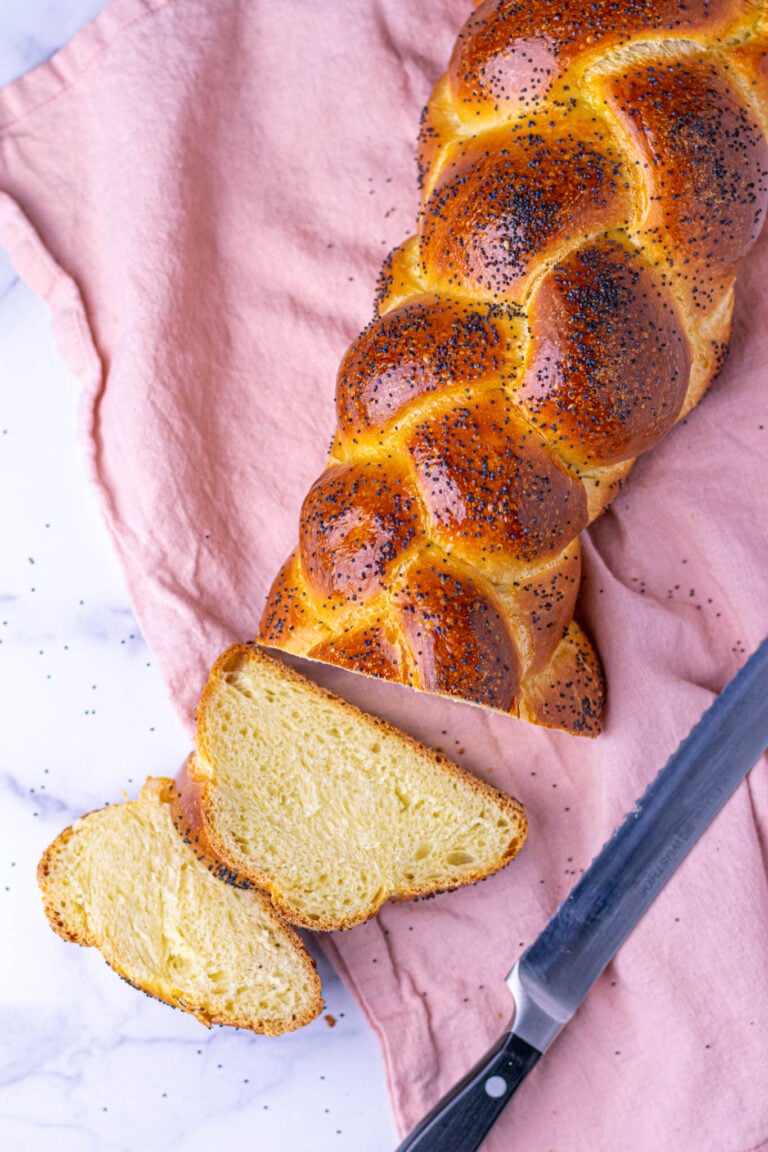 Sourdough challah with poppy seeds on a pink towel and a bread knife.