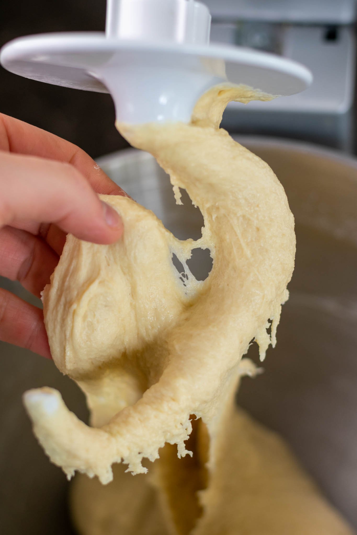 Hand pulling on dough on stand mixer dough hook before adding butter.