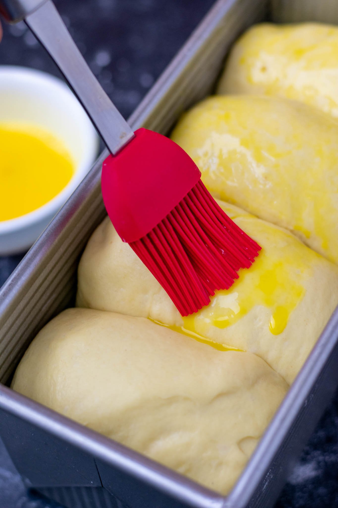 Brushing egg wash onto proofed brioche dough in pan