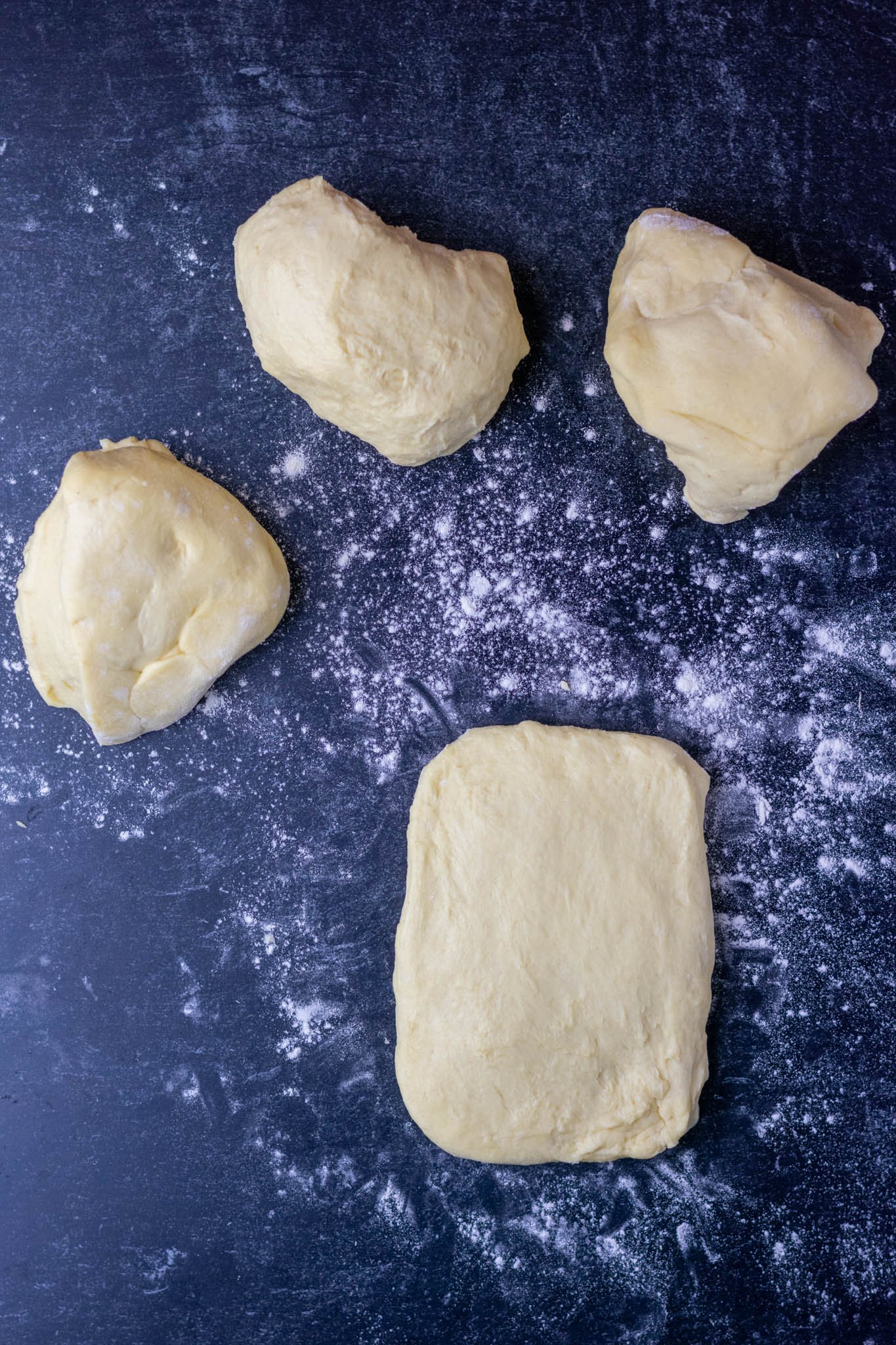 Divided four pieces of sourdough brioche dough on table with flour