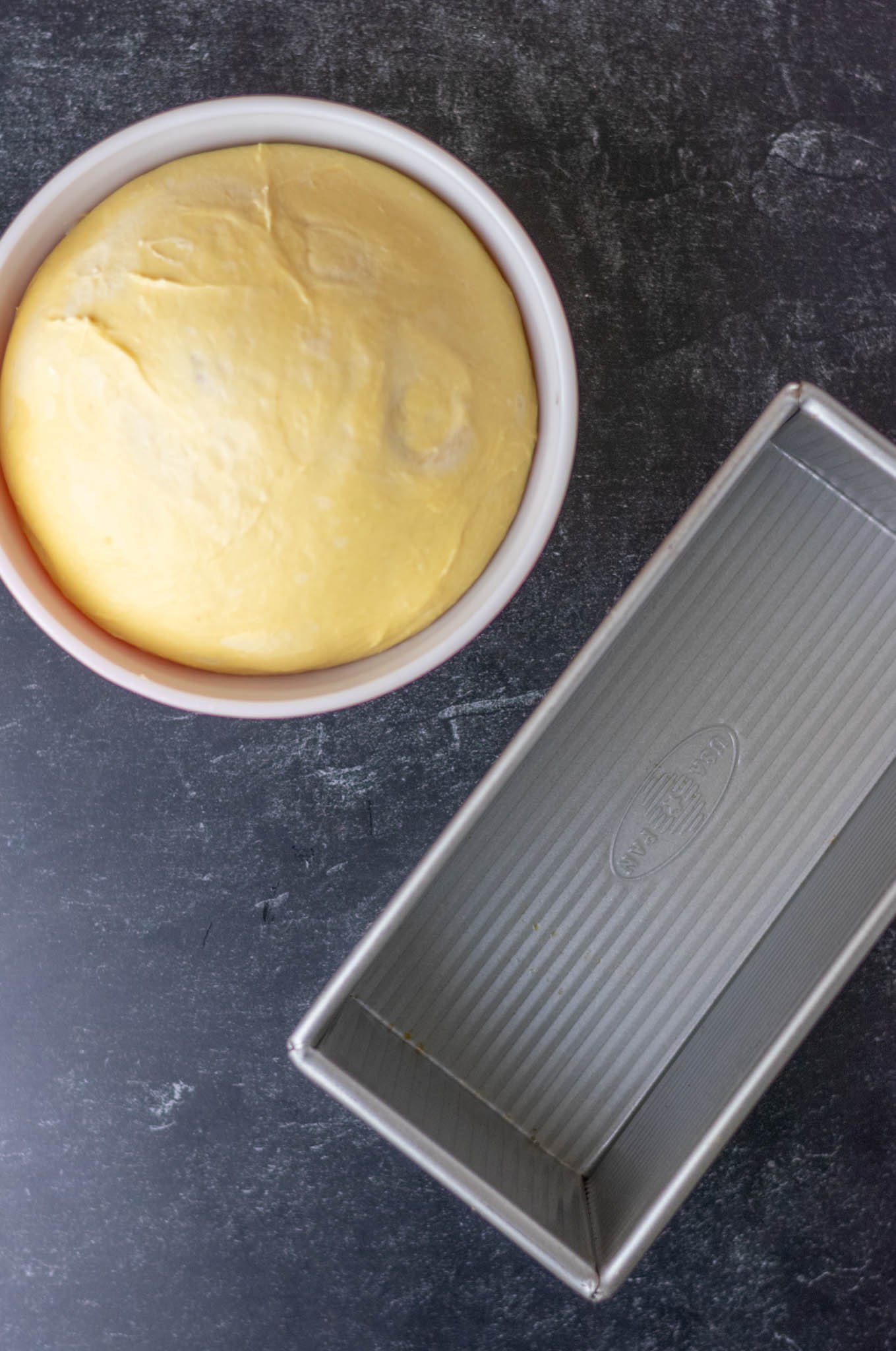 Overhead of bread loaf pan and proofed dough in mixing bowl