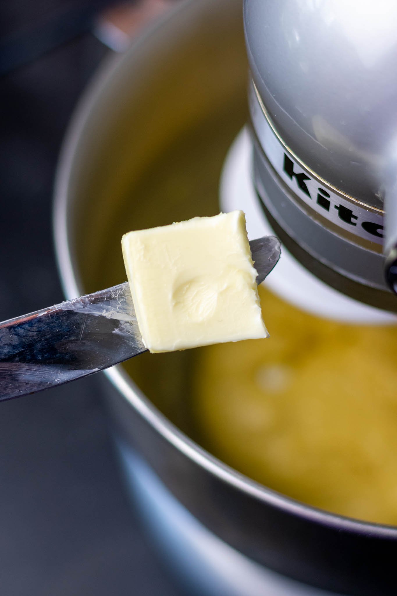Slab of softened butter on butter knife over stand mixer