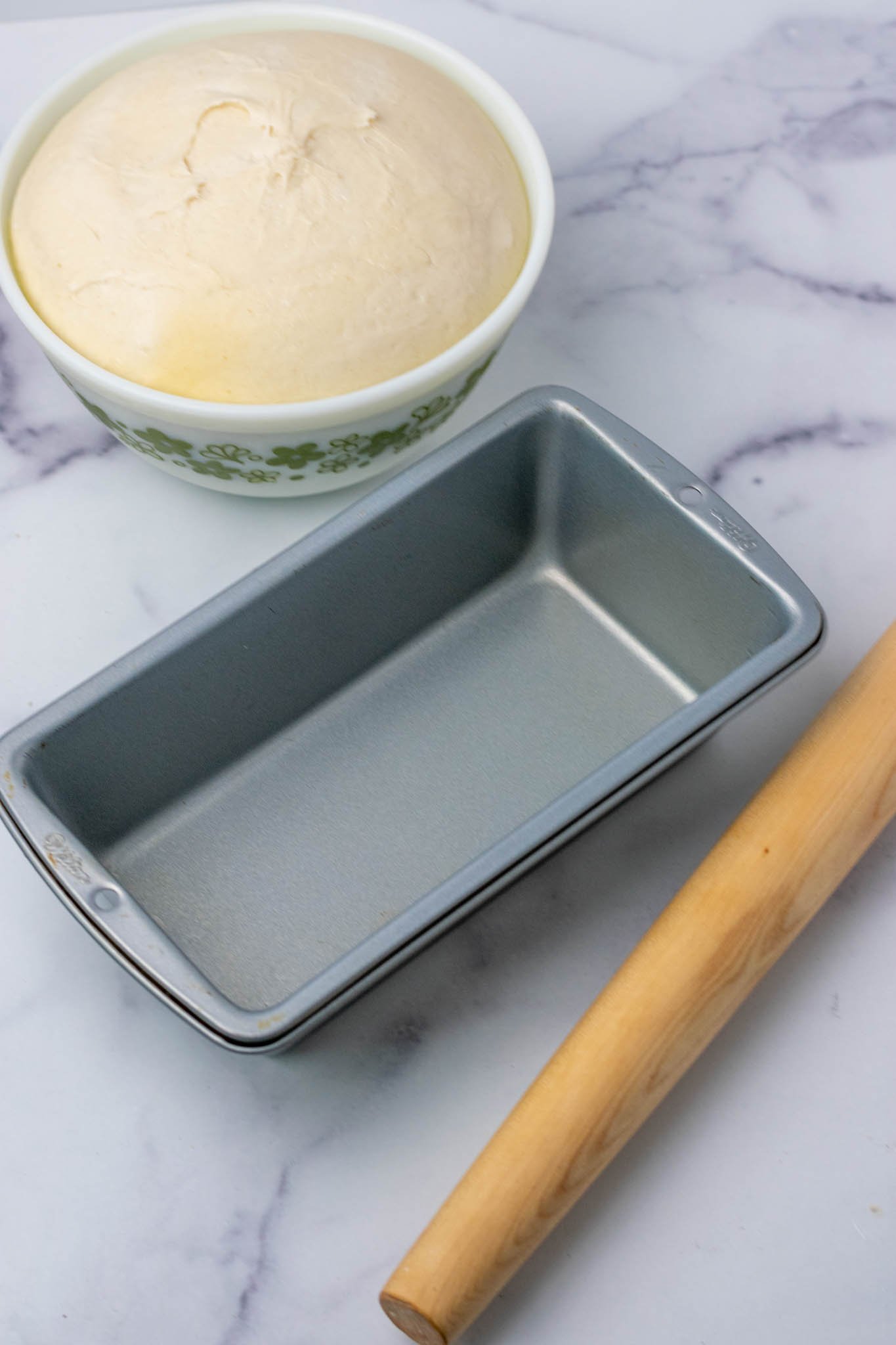 Bread loaf pan, rolling pin, and proofed sourdough sandwich bread dough in bowl