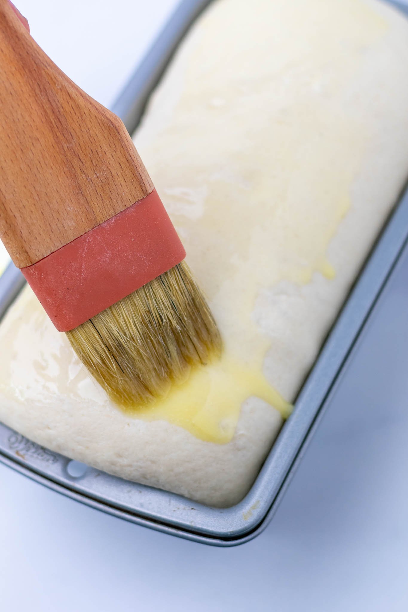 Brushing melted butter onto proofed sourdough sandwich bread in pan