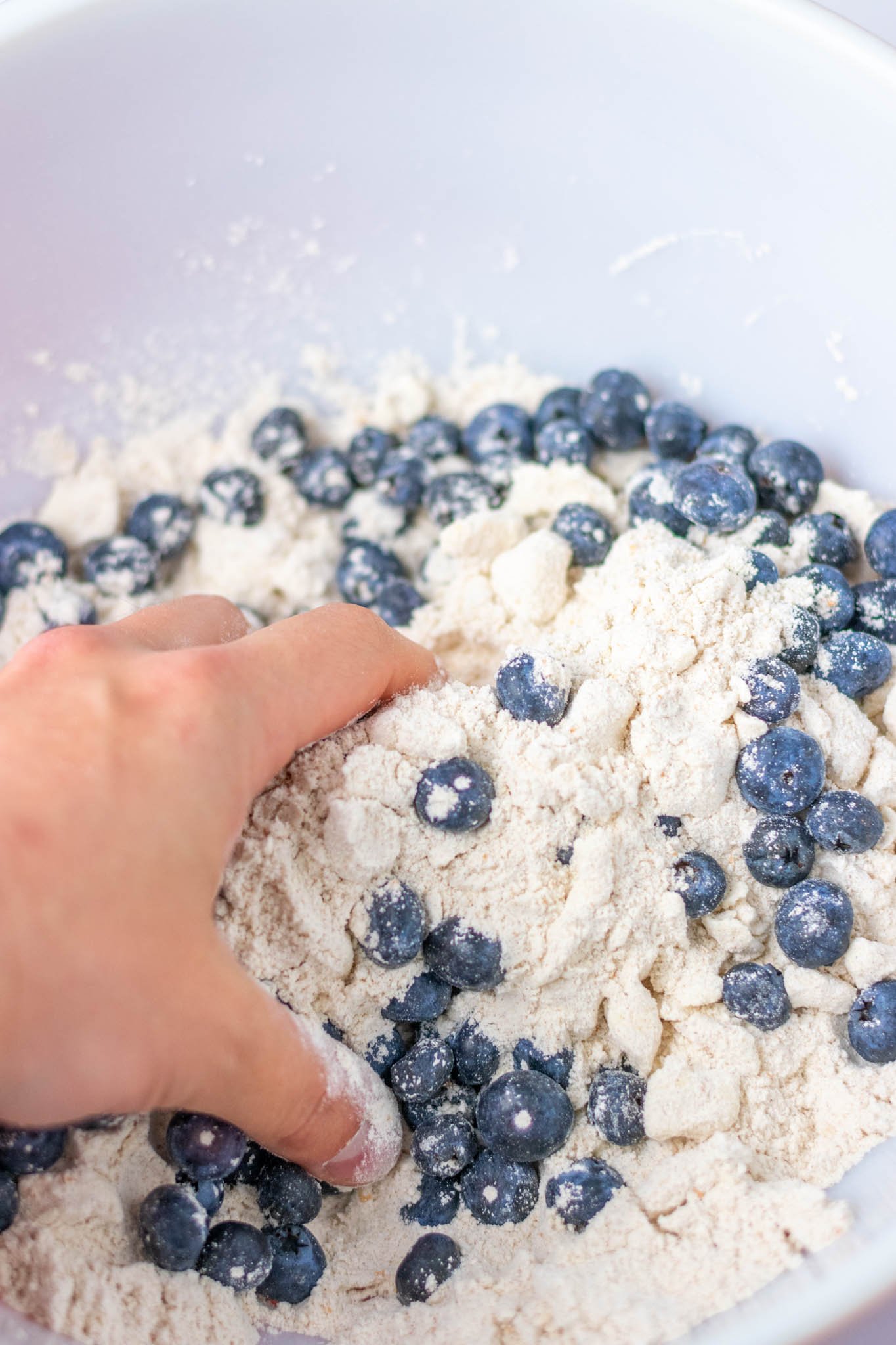 Hand in bowl mixing together blueberries and scone ingredients