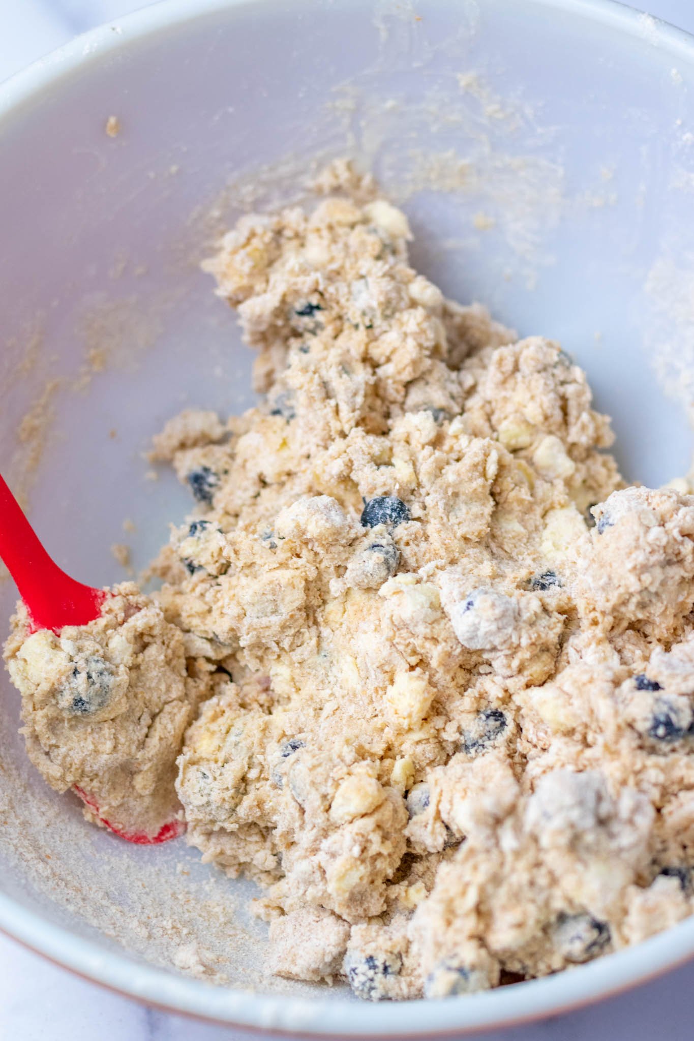 Mixing blueberry scone mixture together with spatula in bowl
