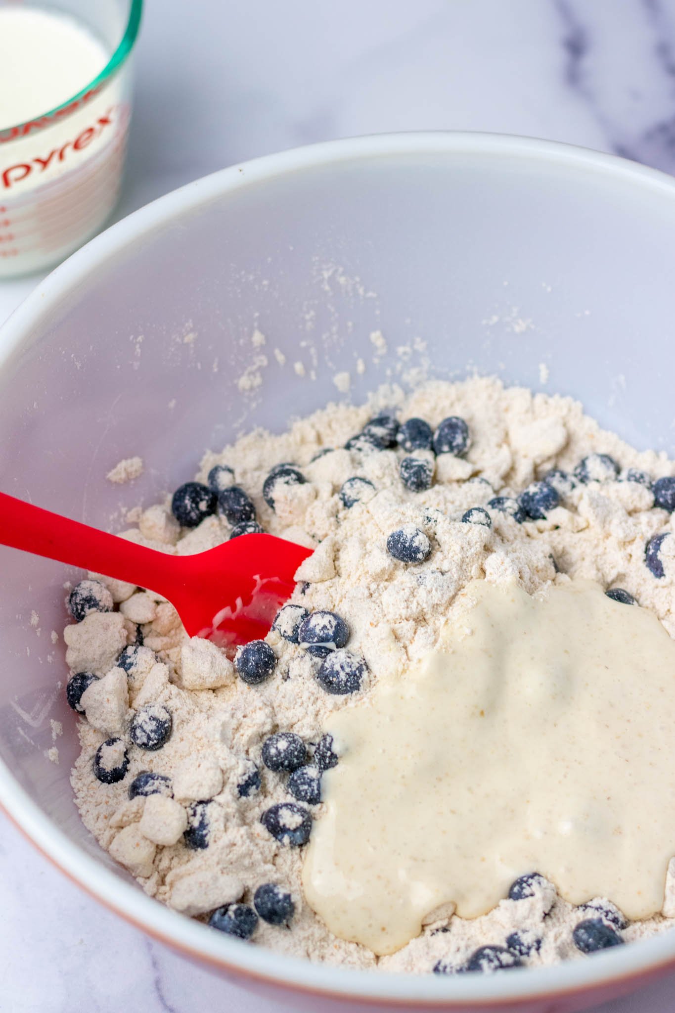 Sourdough discard on top of scone dough with blueberries in bowl before mixing