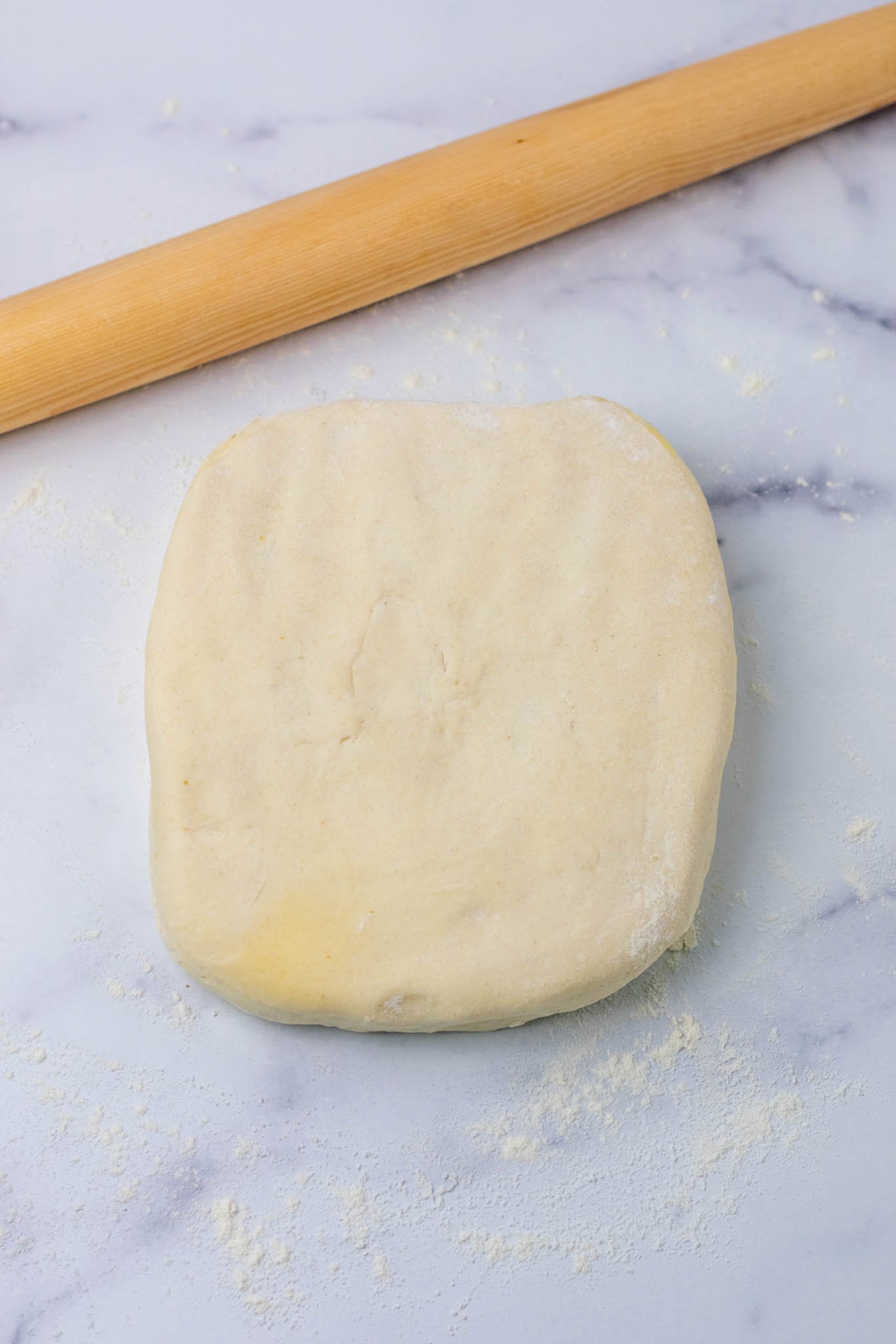 Sourdough sandwich bread dough patted down into square on counter with rolling pin