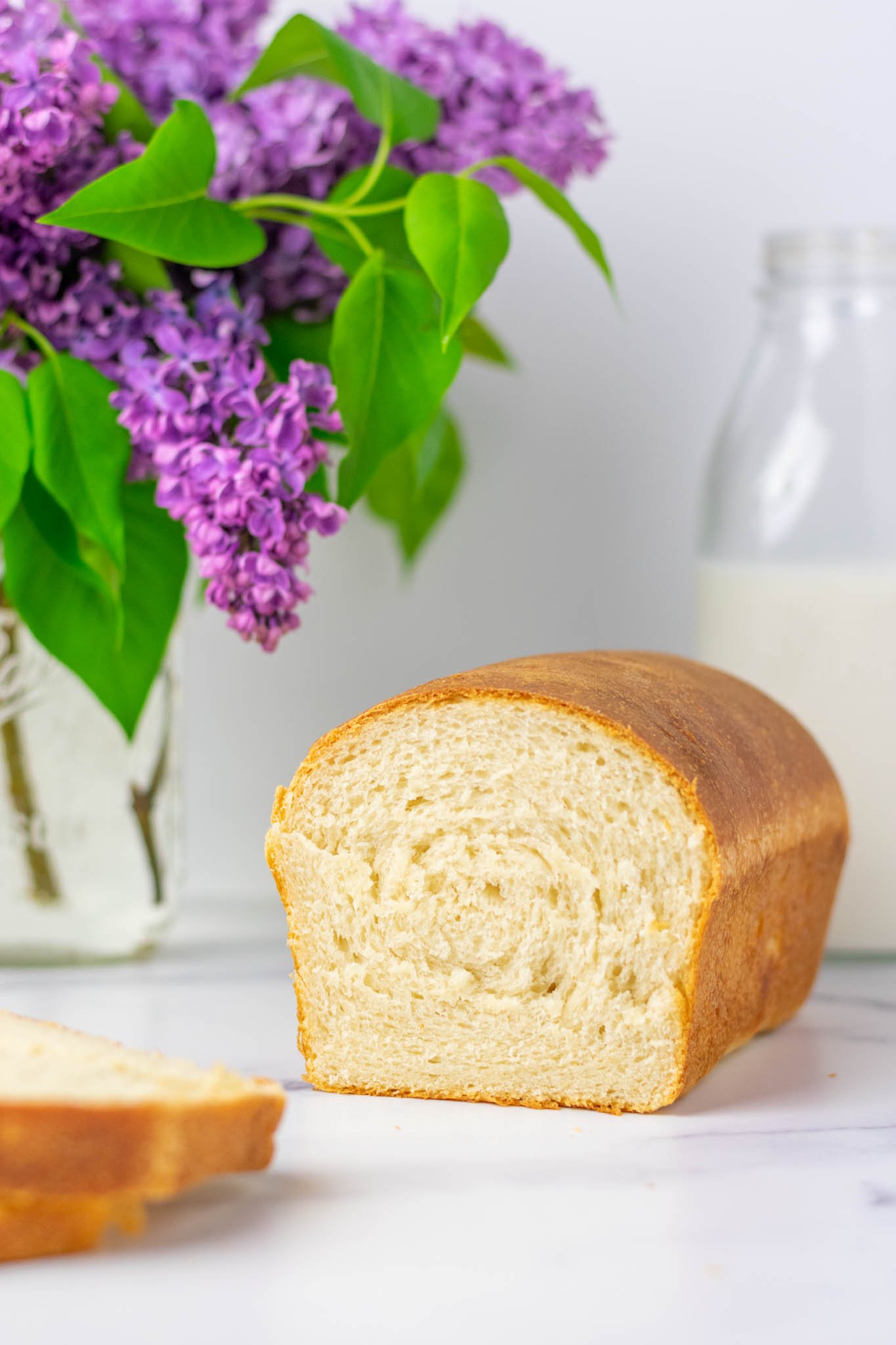 Loaf of sourdough sandwich bread on counter with lilac flower and milk