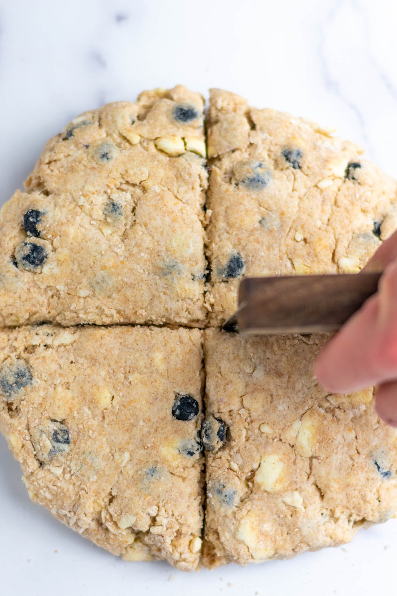 Using bench scraper to divide sourdough discard blueberry scones into four pieces