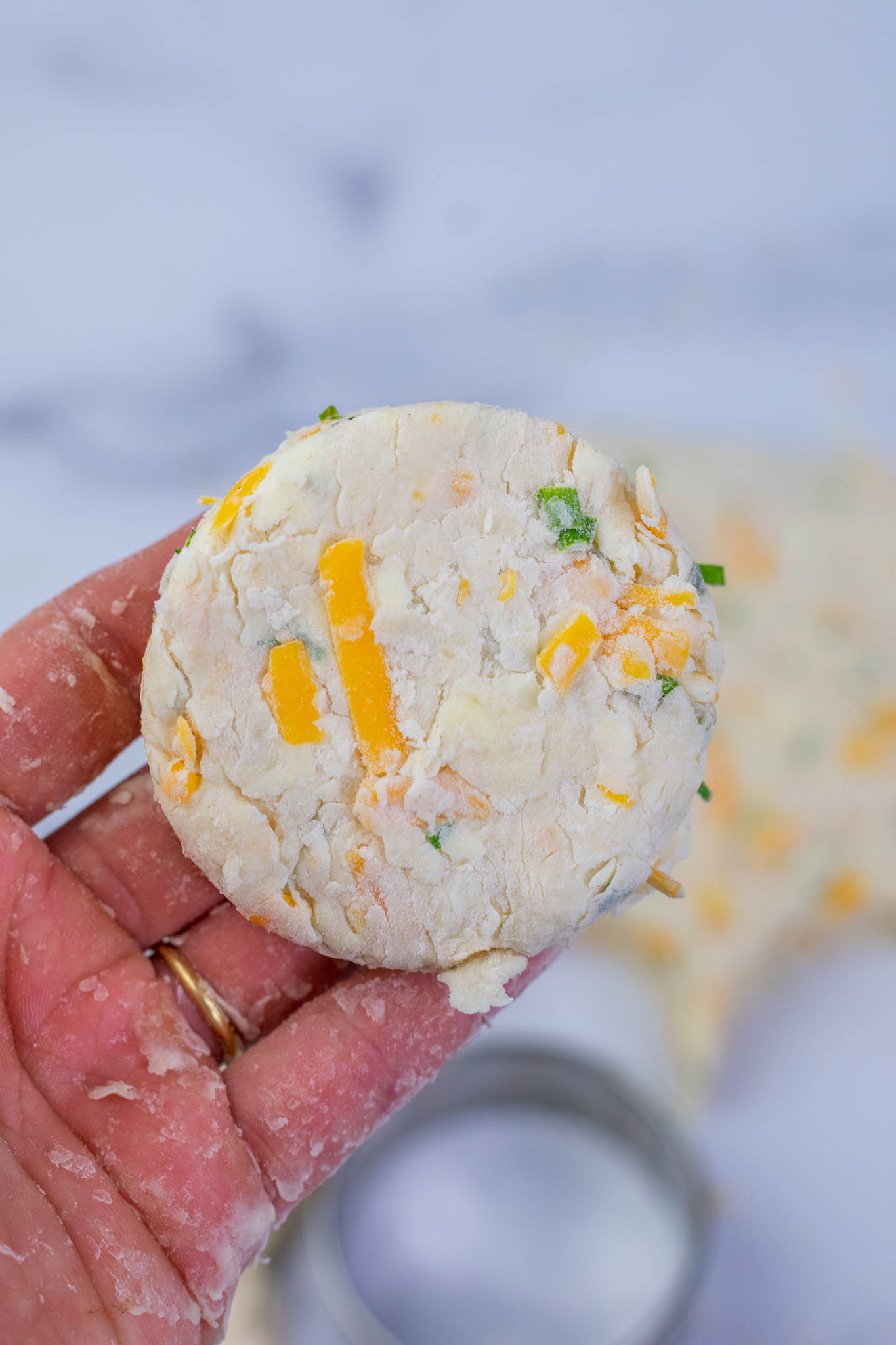 Hand holding a sourdough biscuit with cheddar and chives before baking