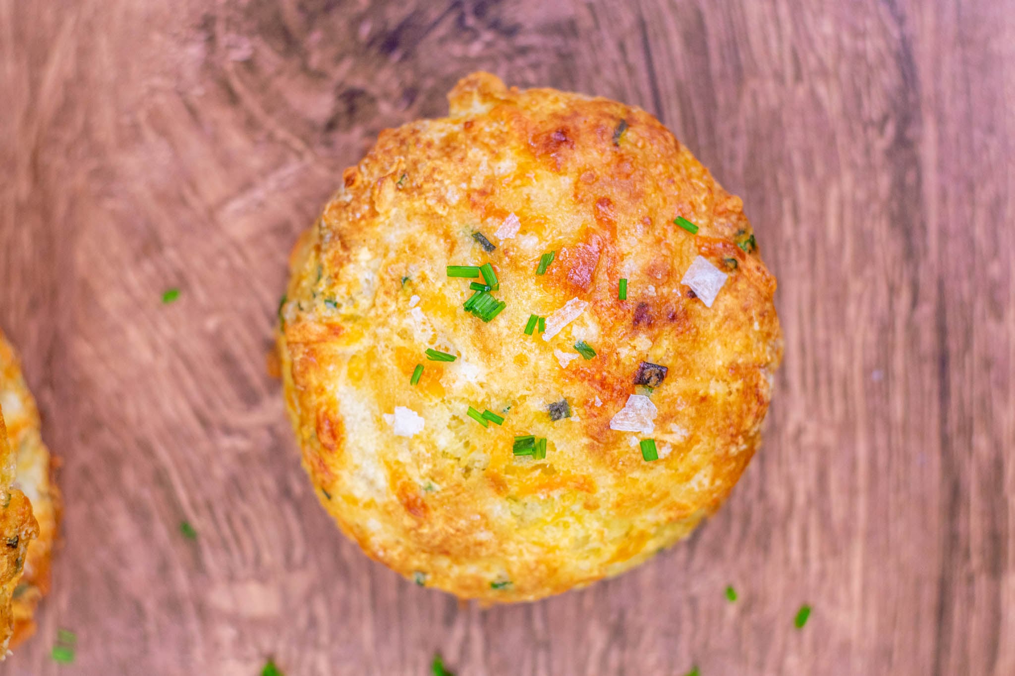 Close up of the top of a  cheddar sourdough biscuit topped with flaky salt and chives