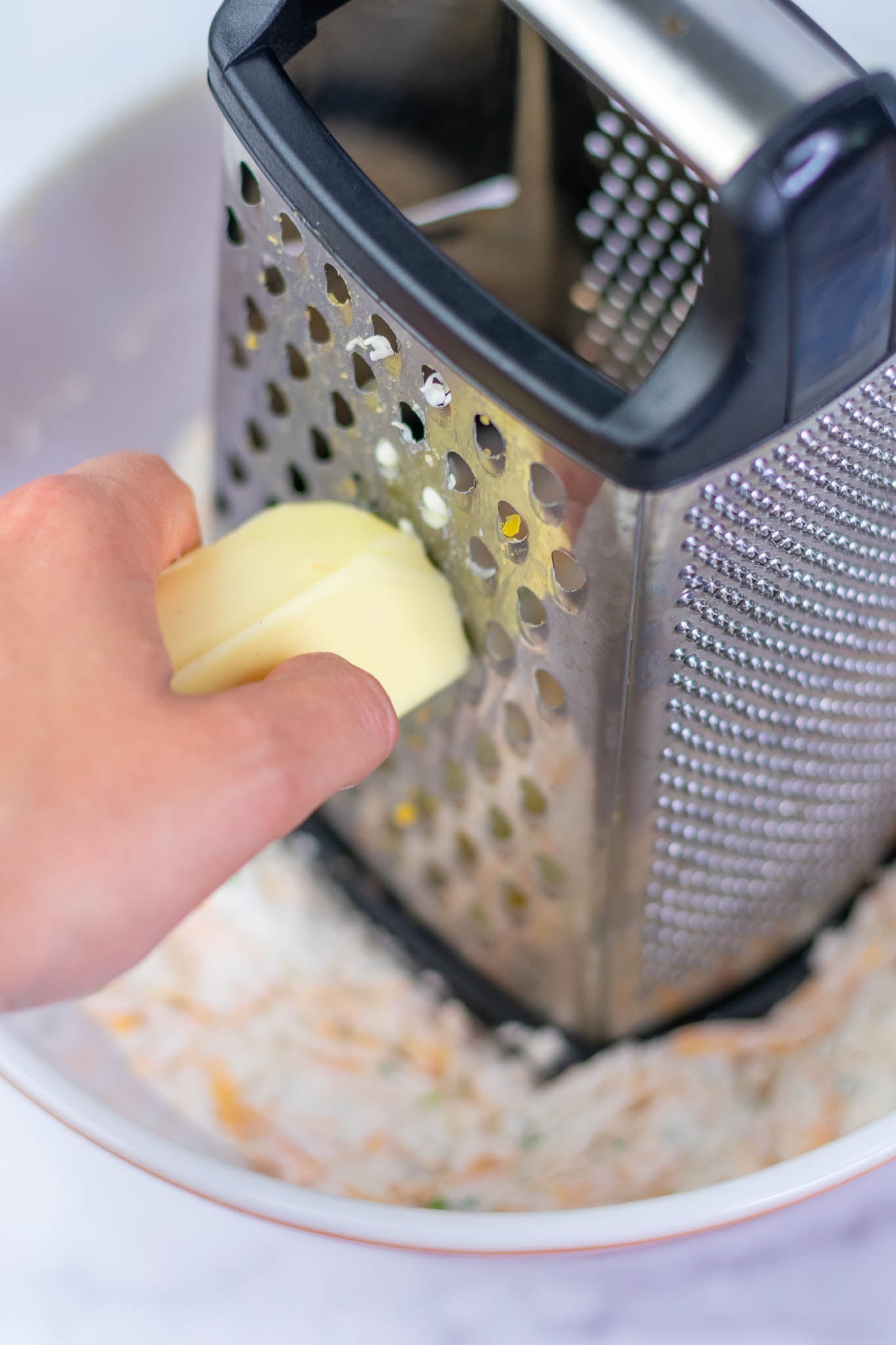 Grating frozen butter on box grater in mixing bowl