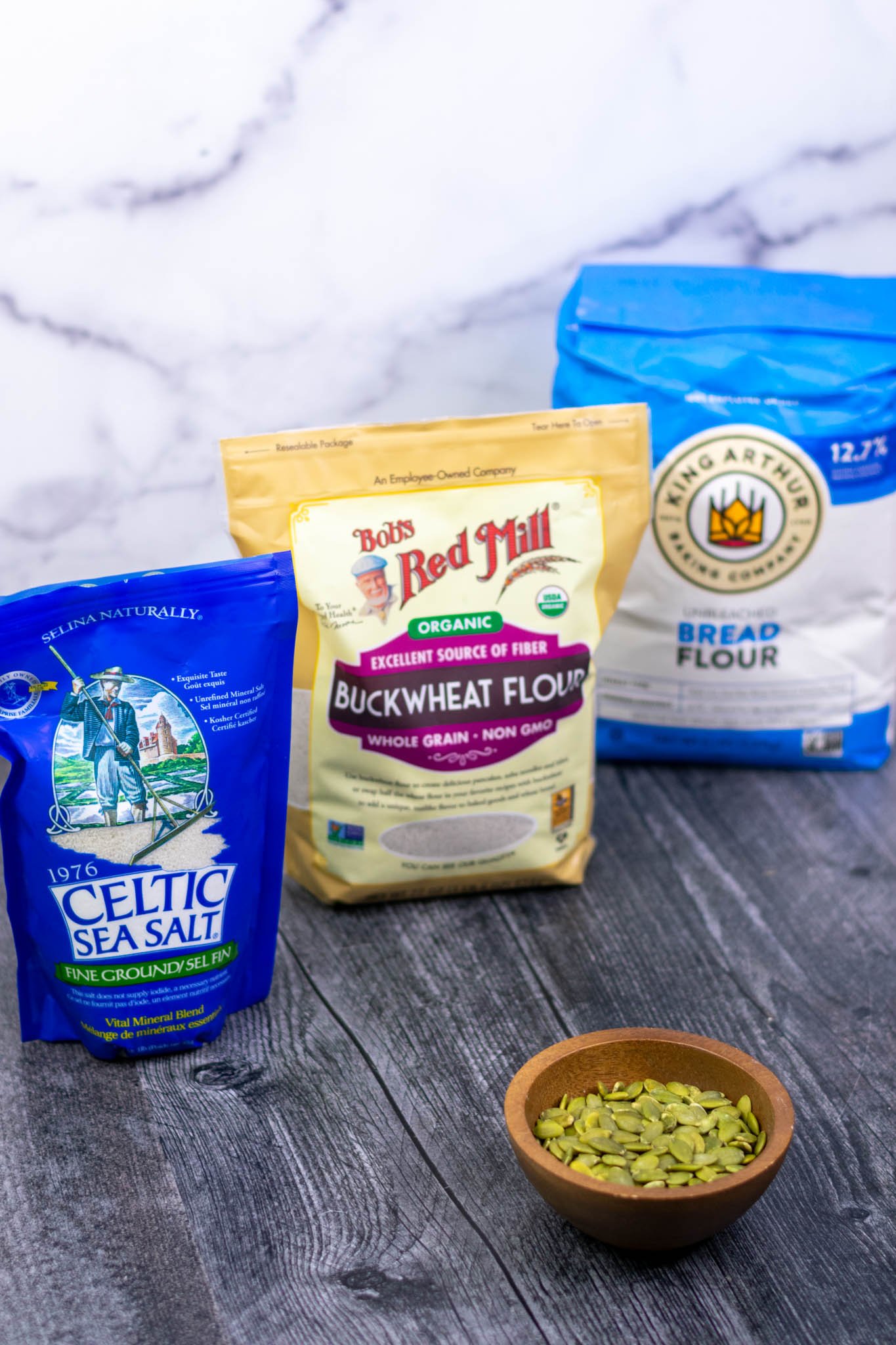 Bags of bread flour, buckwheat flour, sea salt, and bowl of pumpkin seeds