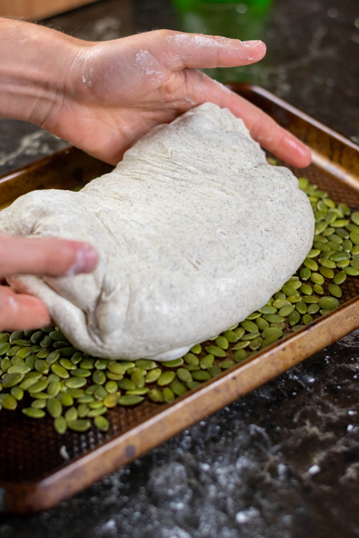 Hands laying buckwheat sourdough on pan with pumpkin seeds