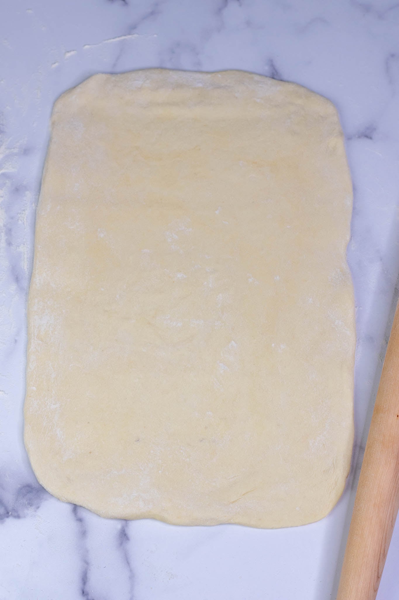 Sourdough cinnamon roll brioche dough rolled out into a rectangle with rolling pin on counter