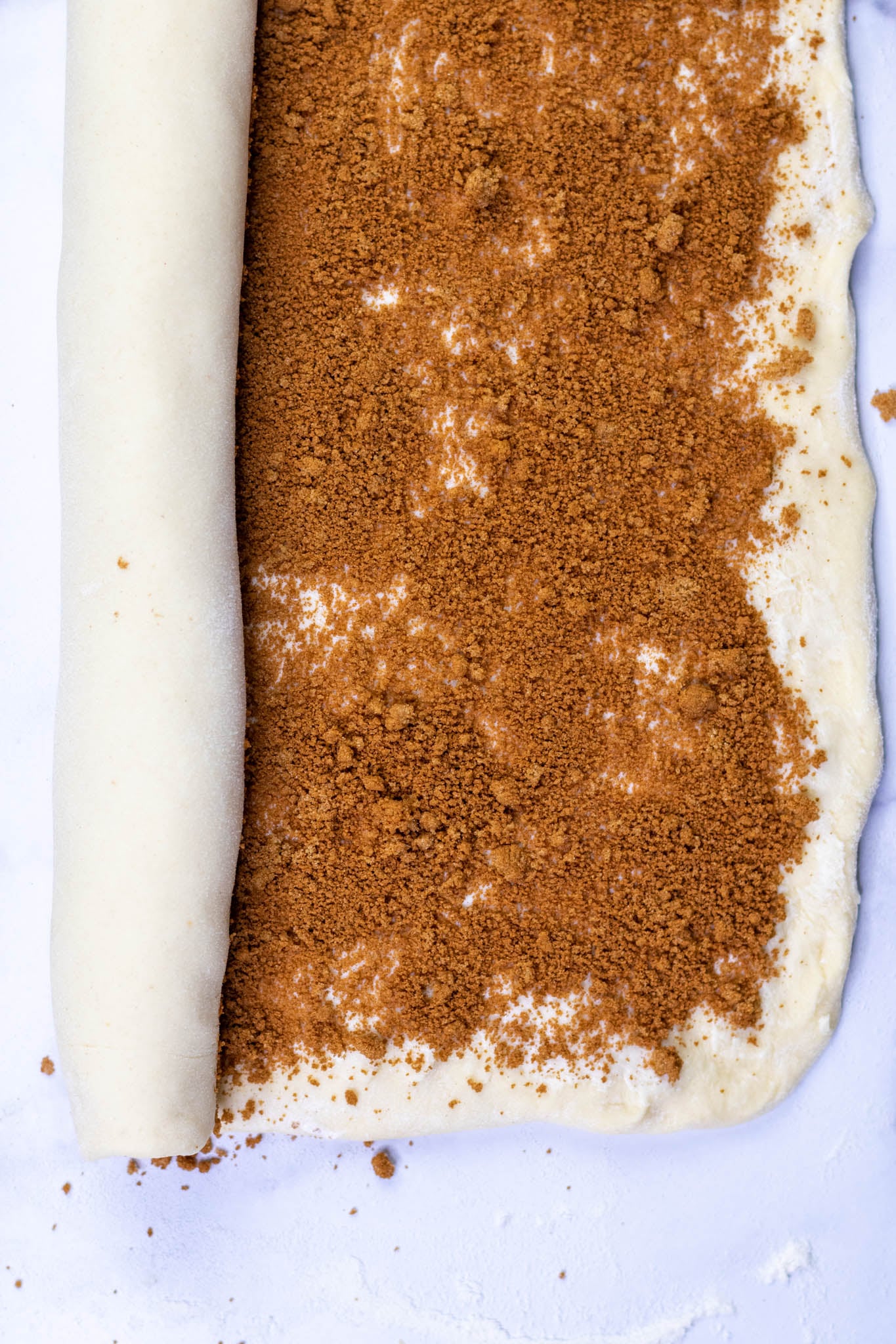 Rolling up Sourdough cinnamon roll brioche dough with cinnamon sugar filling into a log