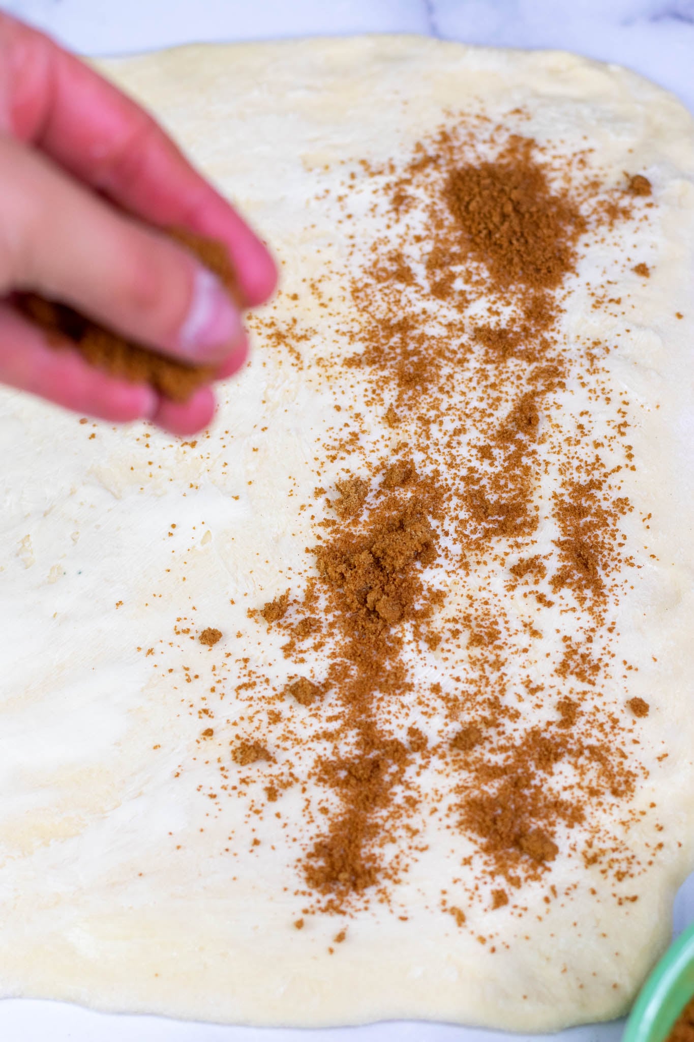 Sprinkling cinnamon sugar filling on rolled out sourdough brioche dough