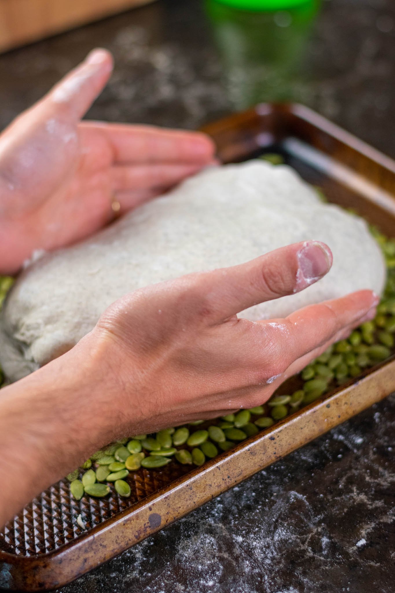 Hands topping buckwheat sourdough with pumpkin seeds in sheet pan