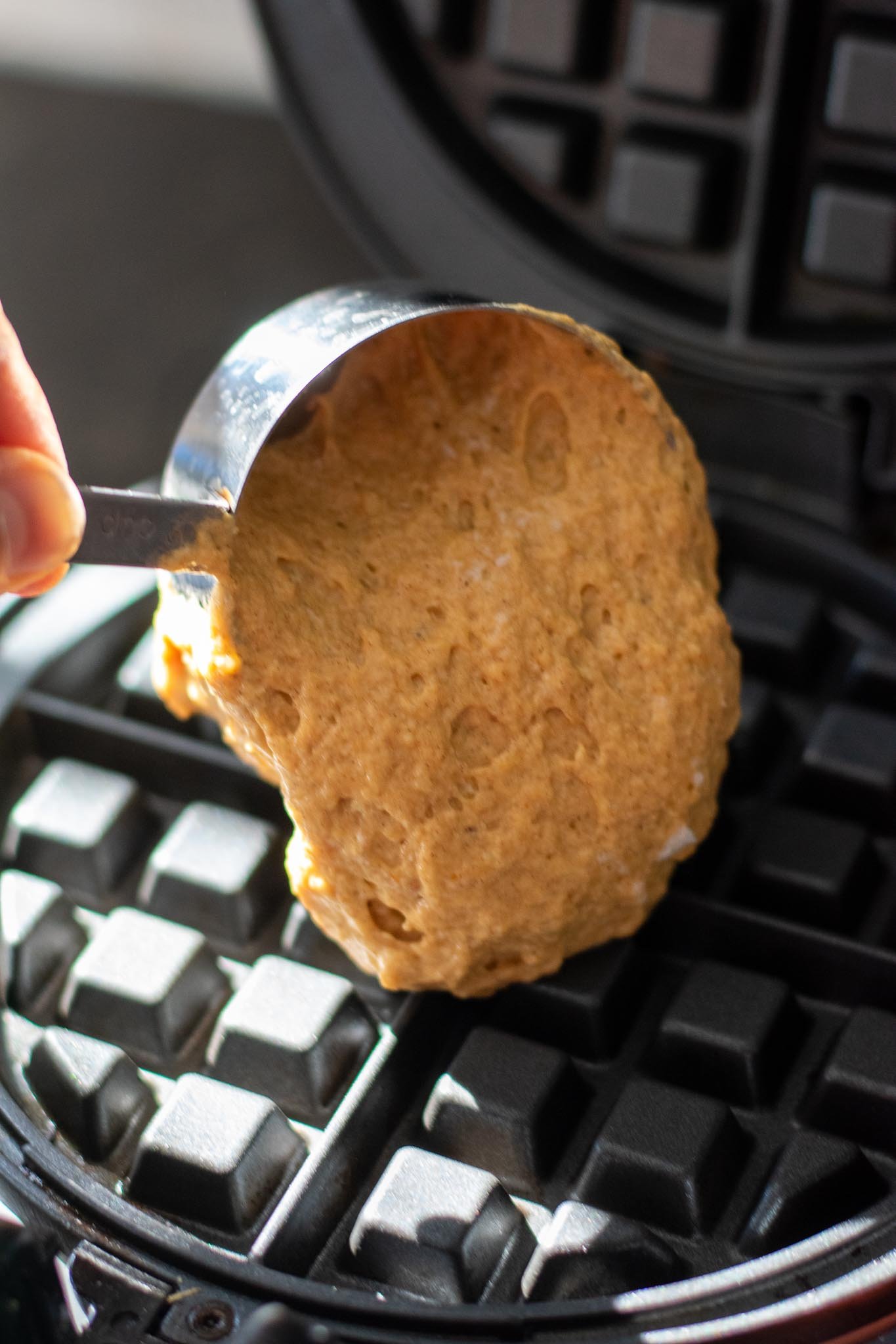 Pouring a half cup of Sourdough Pumpkin Waffles batter on waffle iron