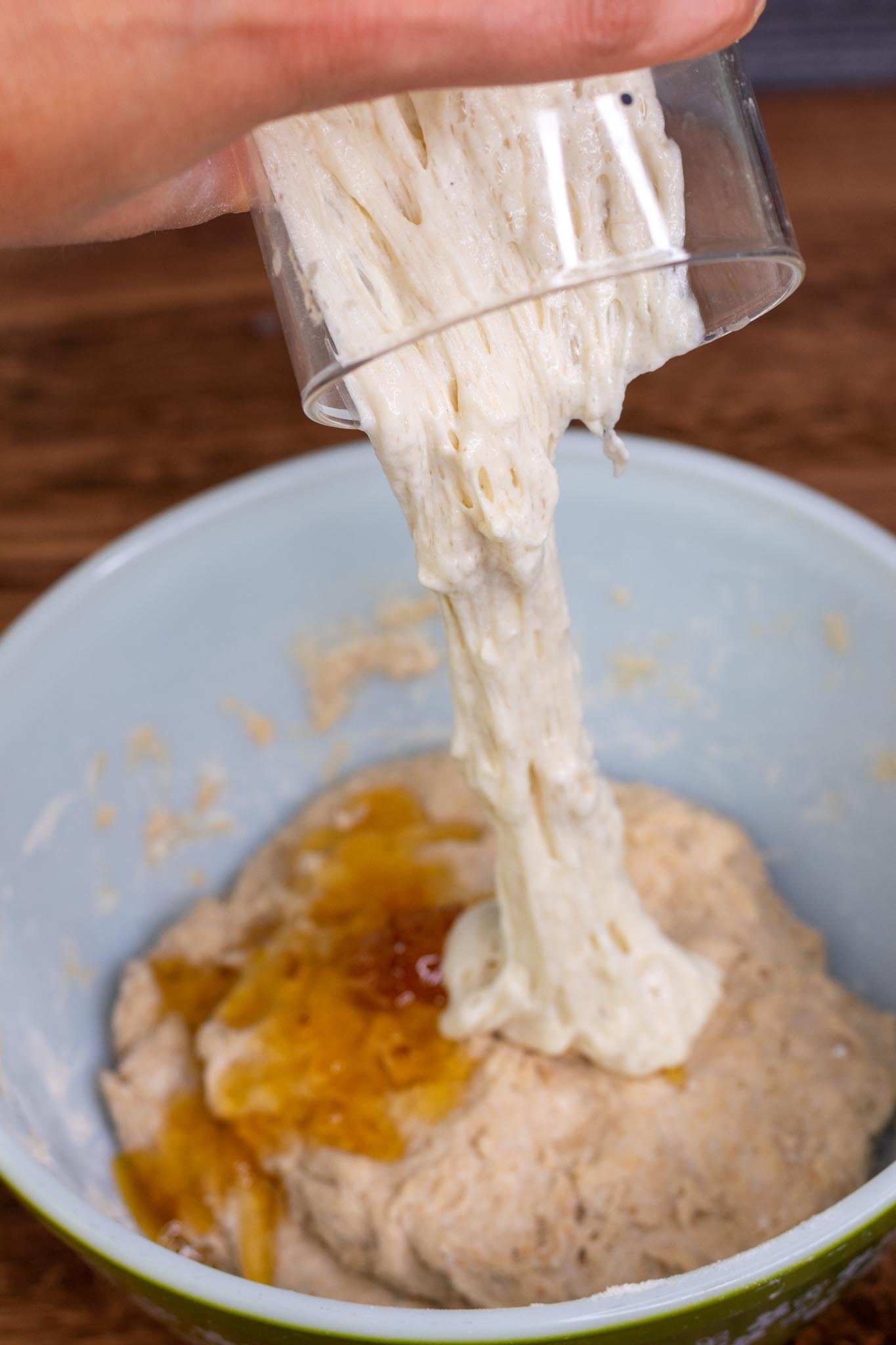 Pouring jar of sourdough starter or levain into dough with honey