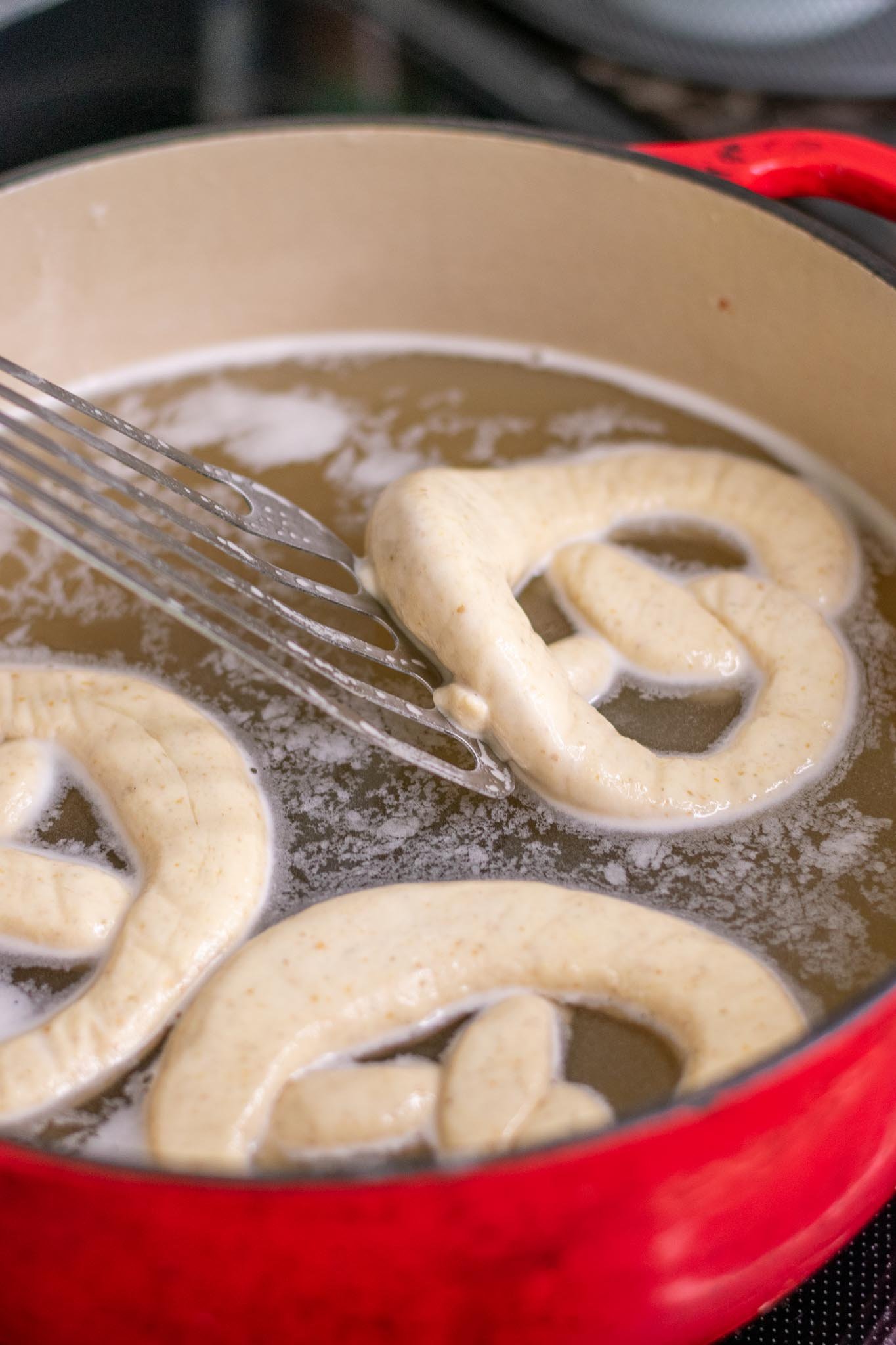 Flipping sourdough pretzels in their baking soda bath with a spatula