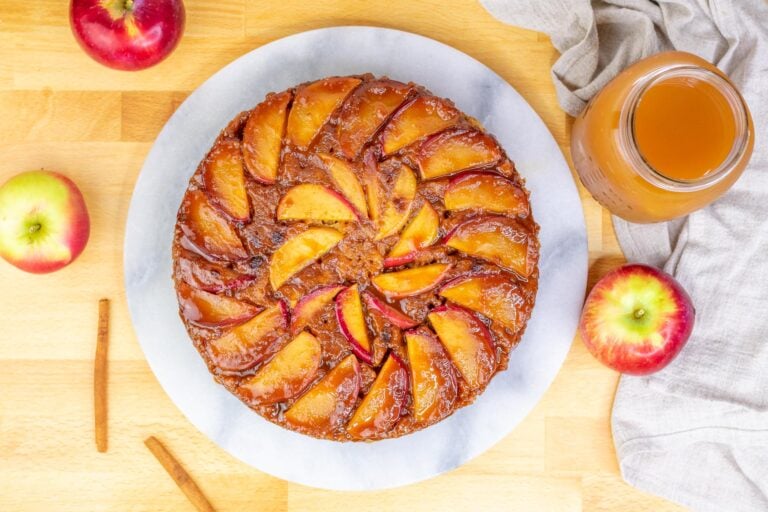 Sourdough apple cider upside-down cake on a platter with apples, cinnamon, and a jar of cider