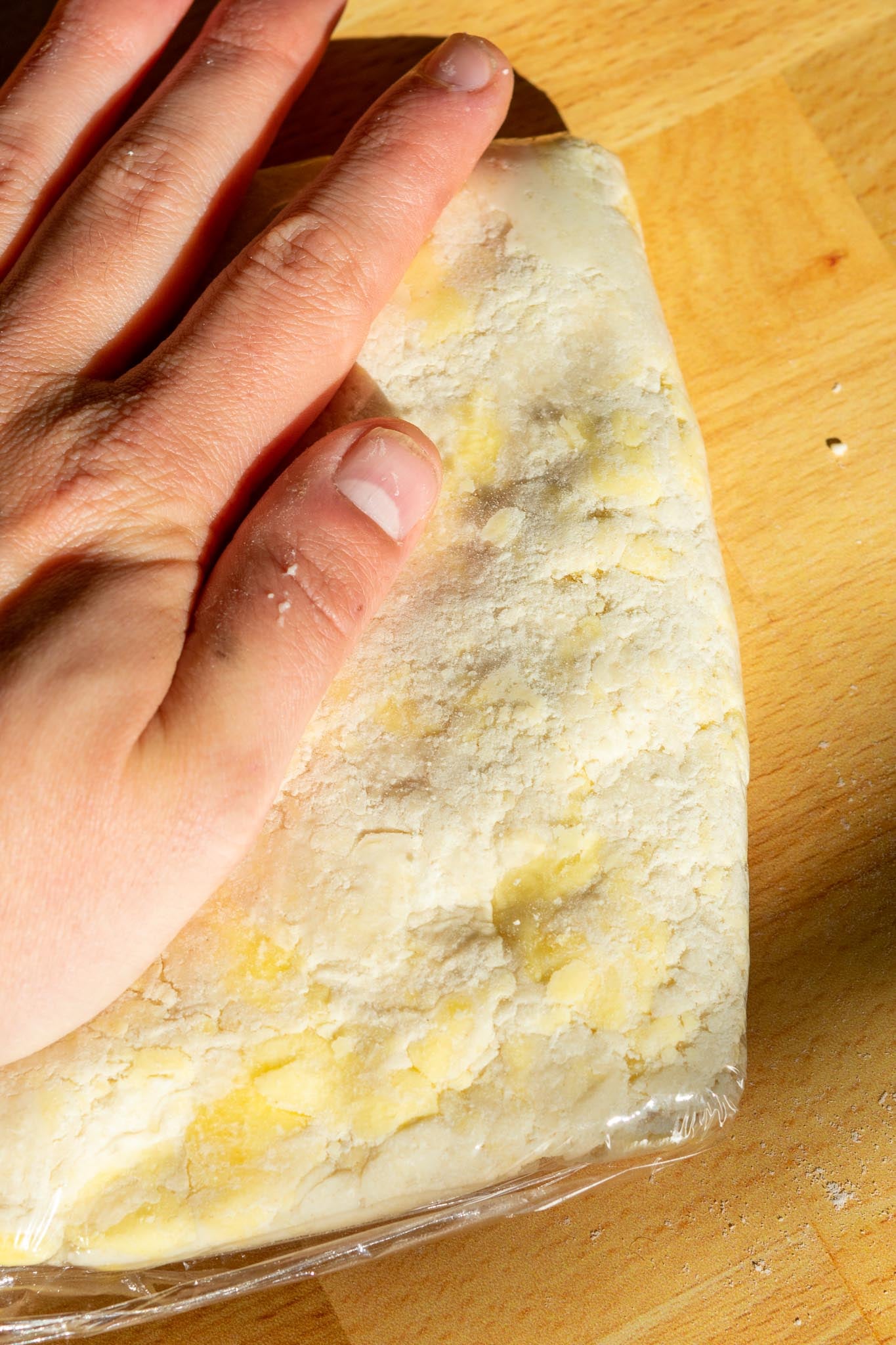 Hand smushing sourdough pie crust in plastic wrap