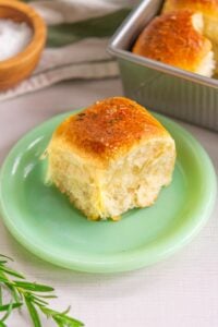 Sourdough dinner rolls with rosemary on plate with a sprig of rosemary and flaky salt