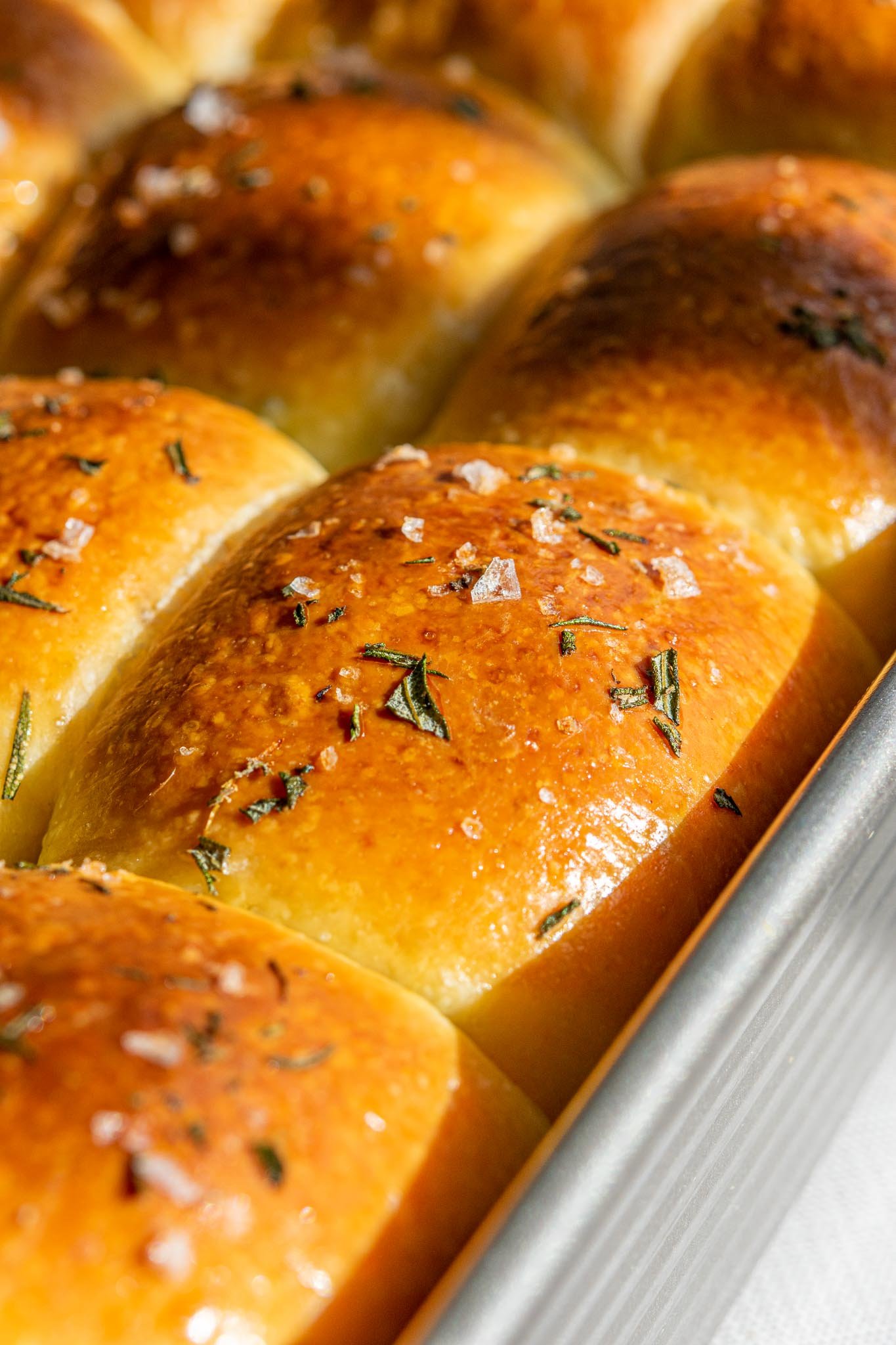 Close up of sourdough dinner rolls baked in pan with rosemary and flaky salt