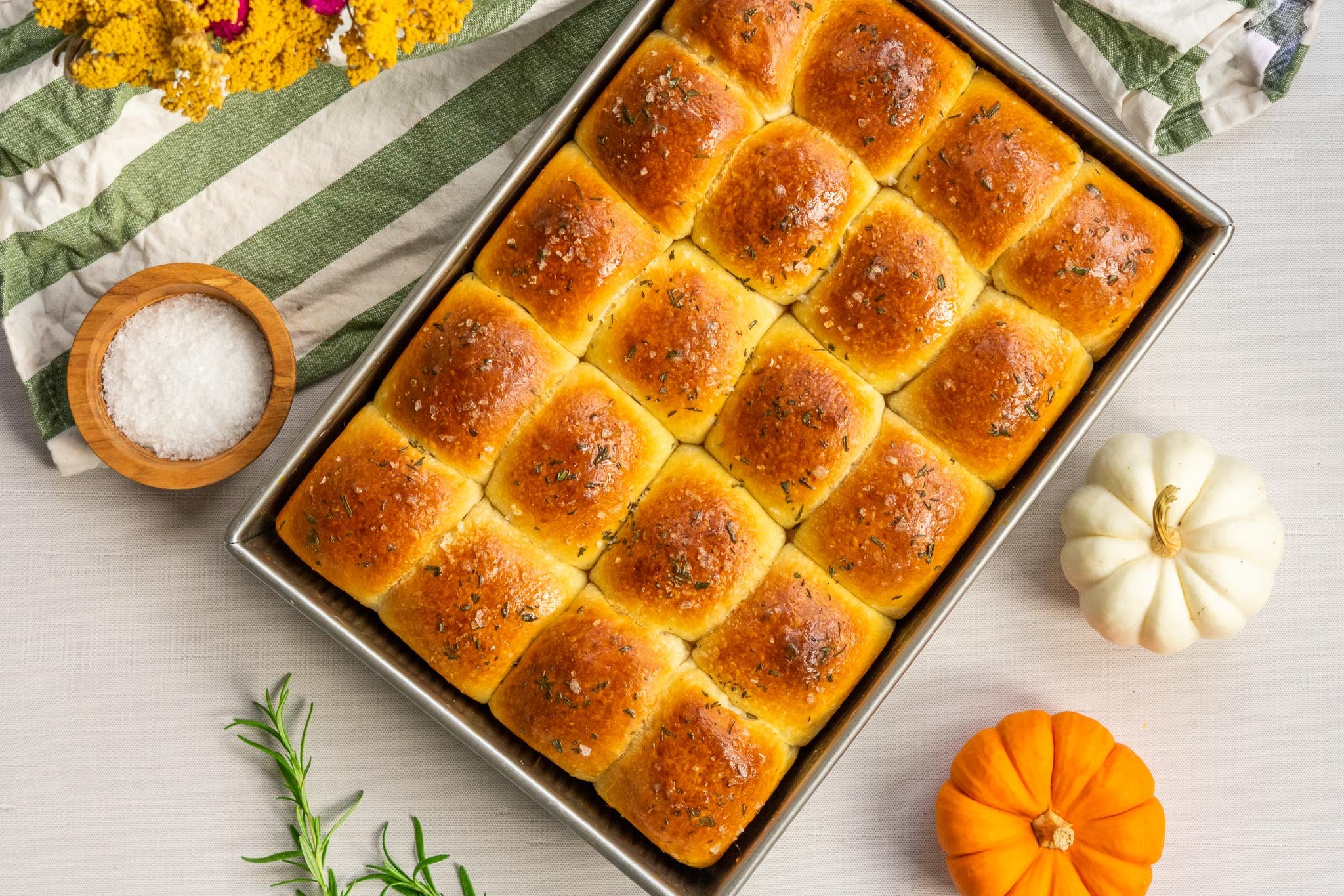 Sourdough Dinner Rolls with Rosemary in pan with pumpkins, salt, rosemary sprigs, and a kitchen towel
