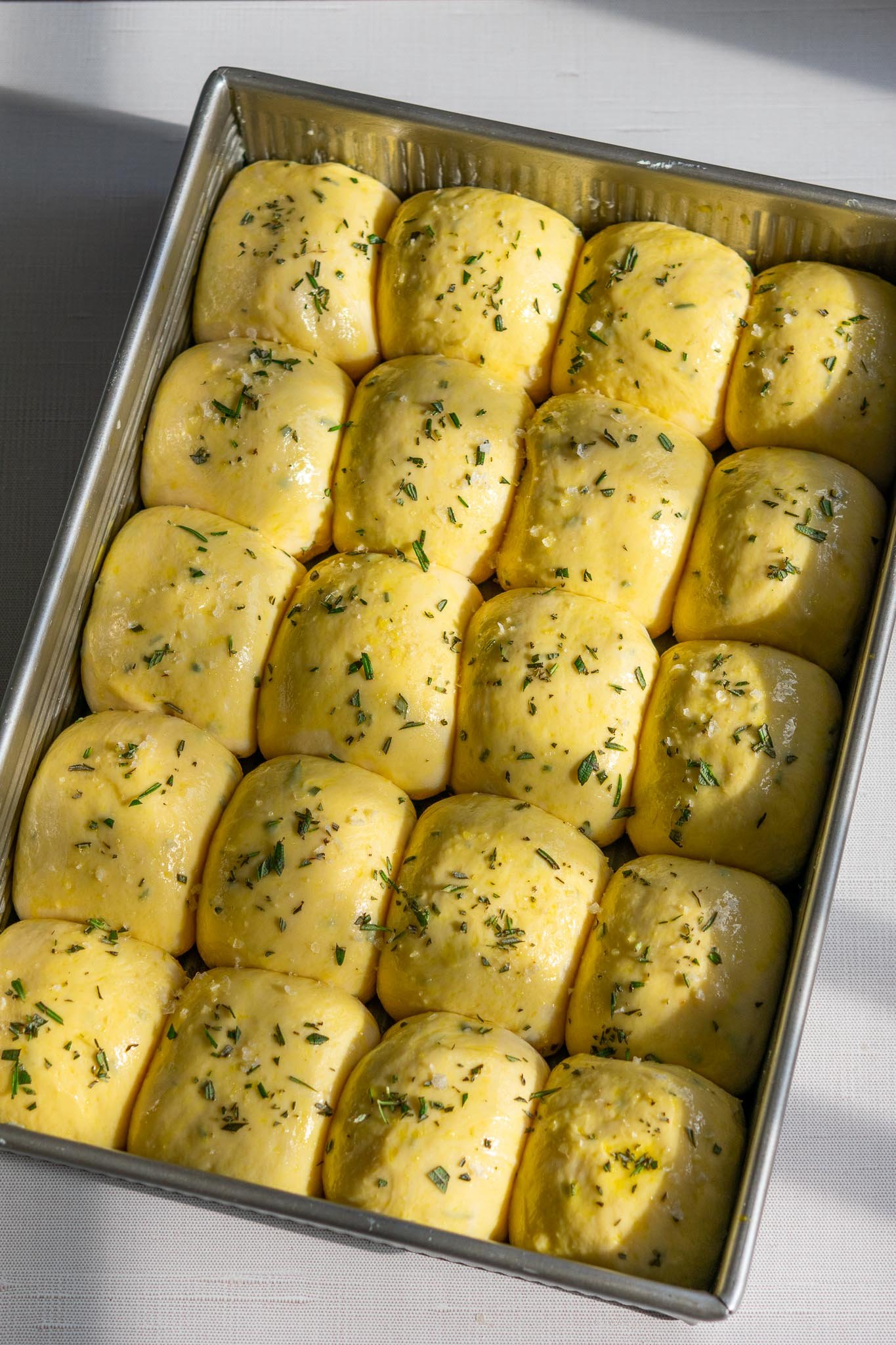 Sourdough Dinner rolls brushed with egg wash and sprinkled with rosemary and flaky salt in pan before baking