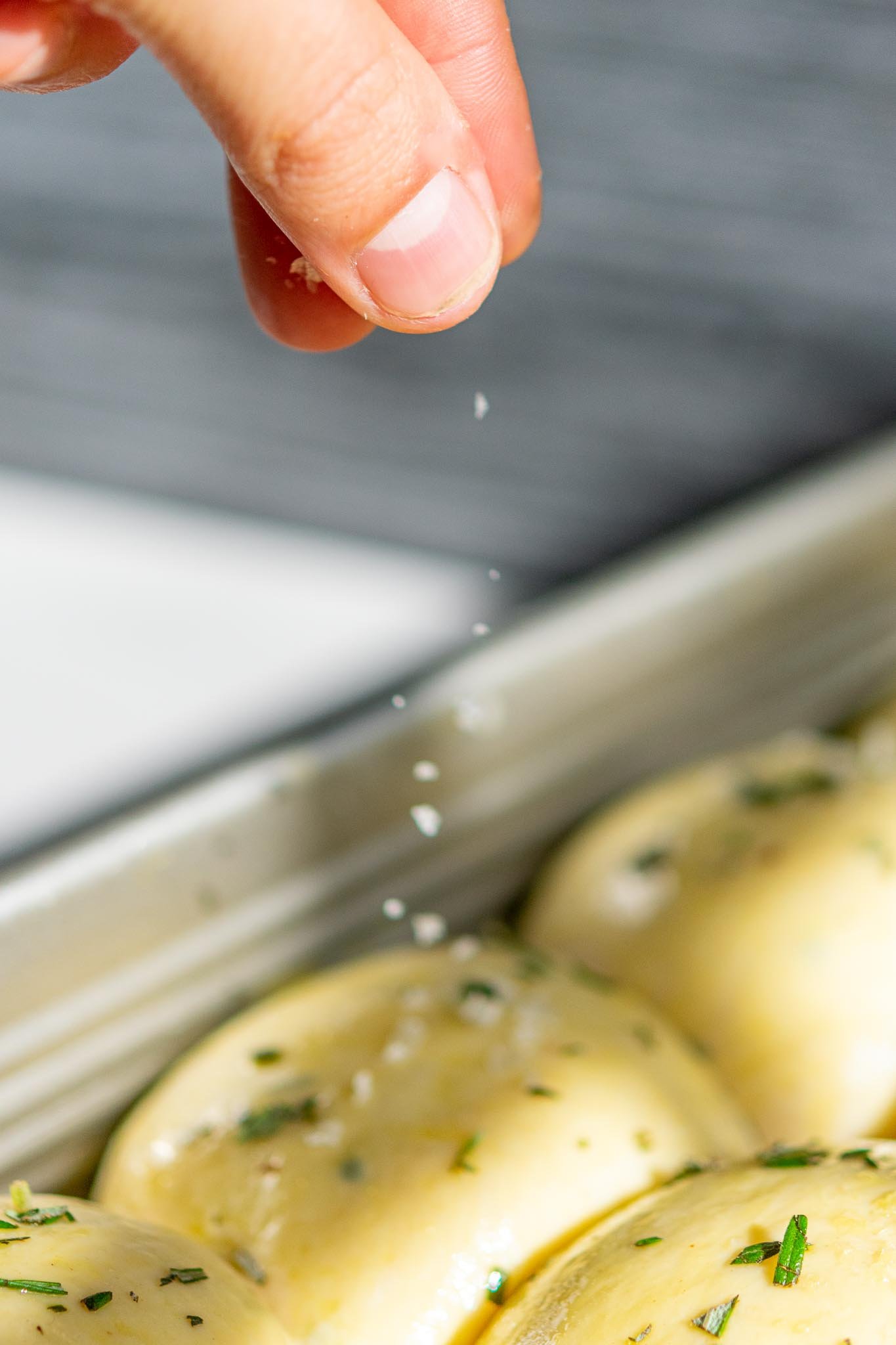 Hand sprinkling flaky salt on dinner rolls mid-air