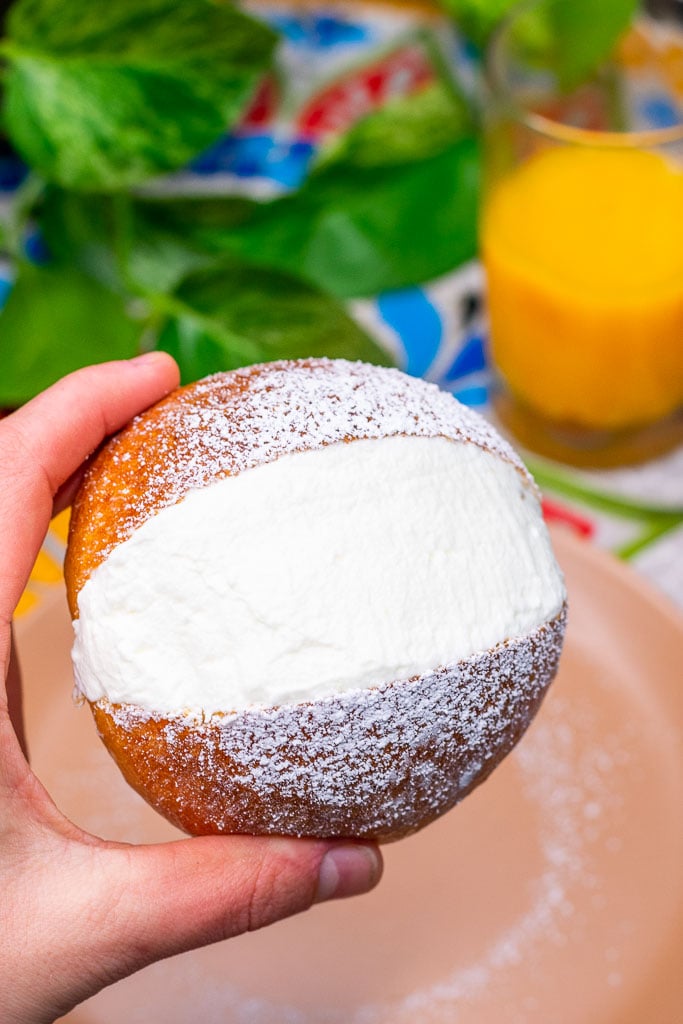 Hand holding a sourdough maritozzo filled with whipped cream and dusted with powdered sugar