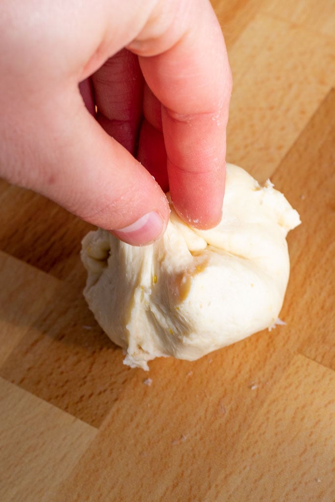 Hand pinching corners of bun together to make a dumpling