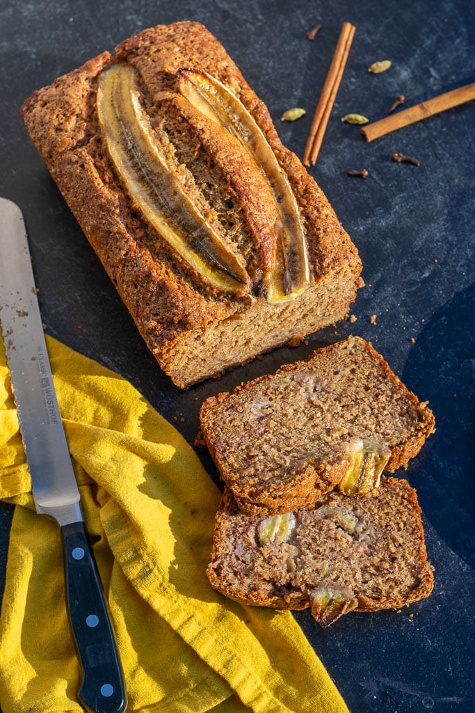 Loaf of sliced sourdough banana bread with a bread knife and chai spices