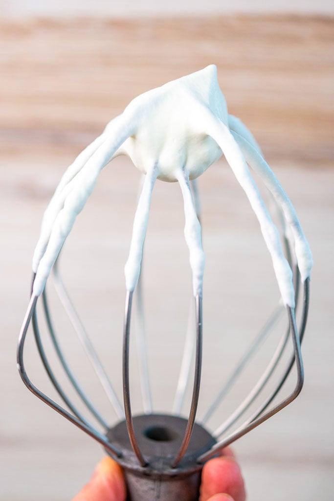 Hand holding a whisk attachment with stiff peaks of whipped cream on it