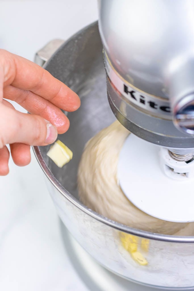 Hand adding a cube of butter to stand mixer with dough