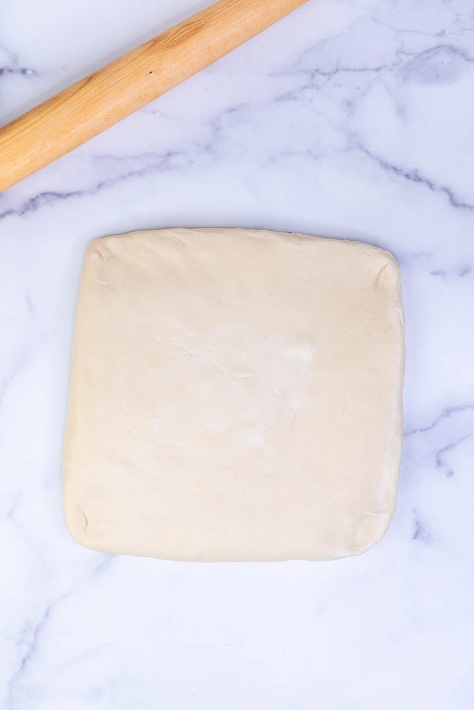 Croissant dough rolled into square with rolling pin