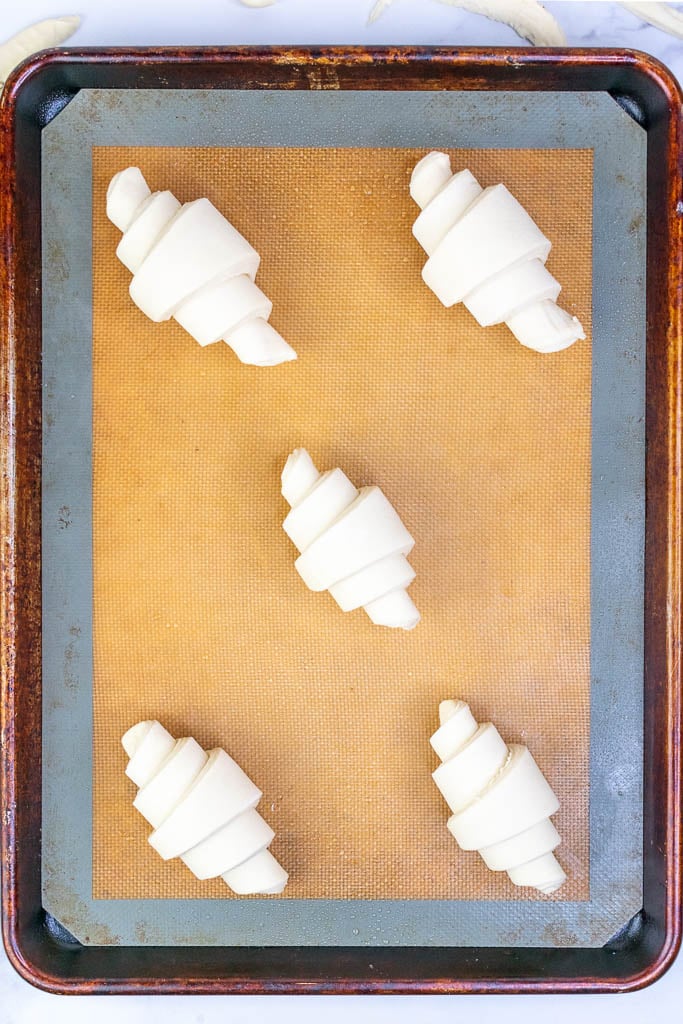 Five shaped sourdough croissants on a baking sheet at the start of final proof